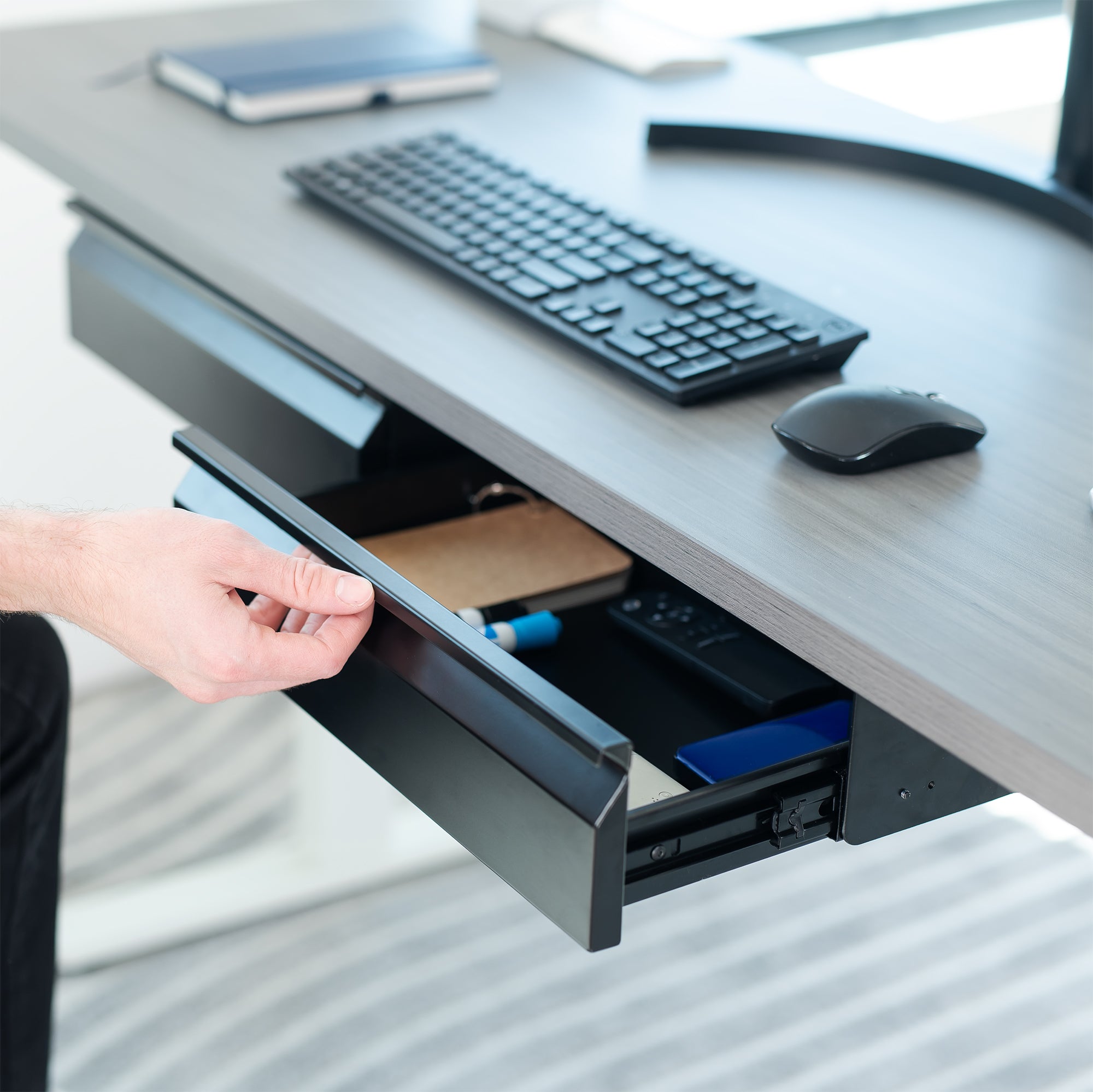 Person opening a desk drawer with office supplies on a desk.