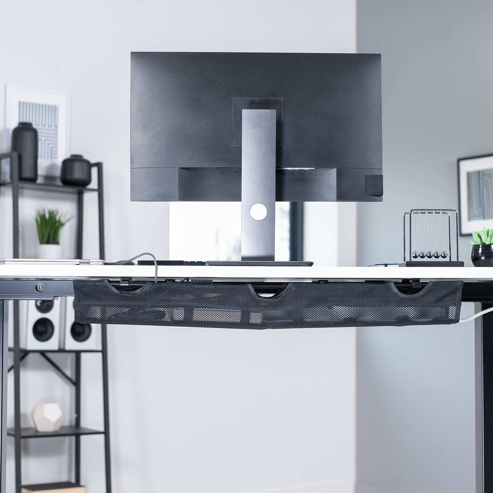 A black mesh cable management system with a power strip holder underneath a desk in a modern office.