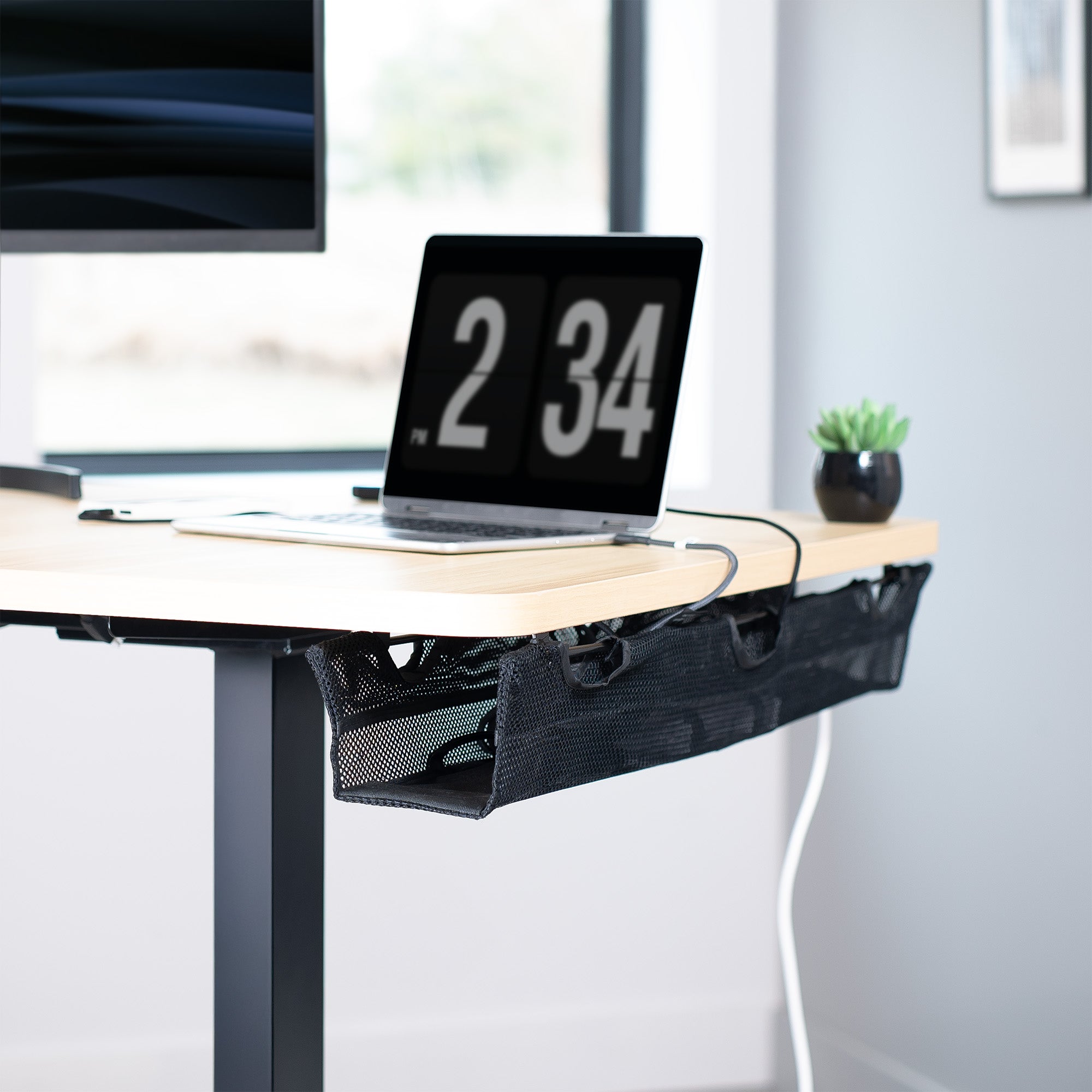 A black mesh cable management system under a desk in a modern home office.