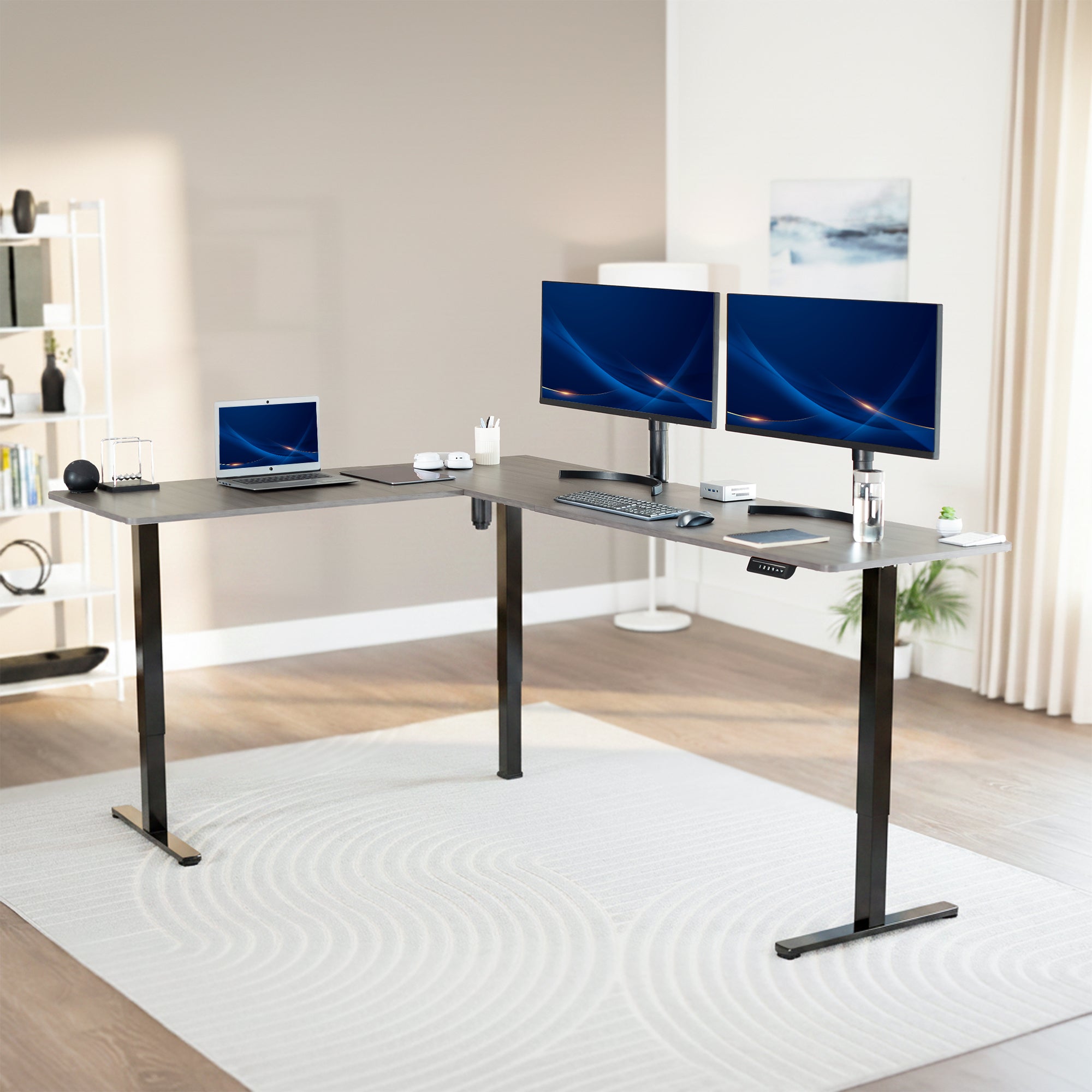 Modern office setup with a standing l-shaped desk, laptop, and two monitors in a bright room.