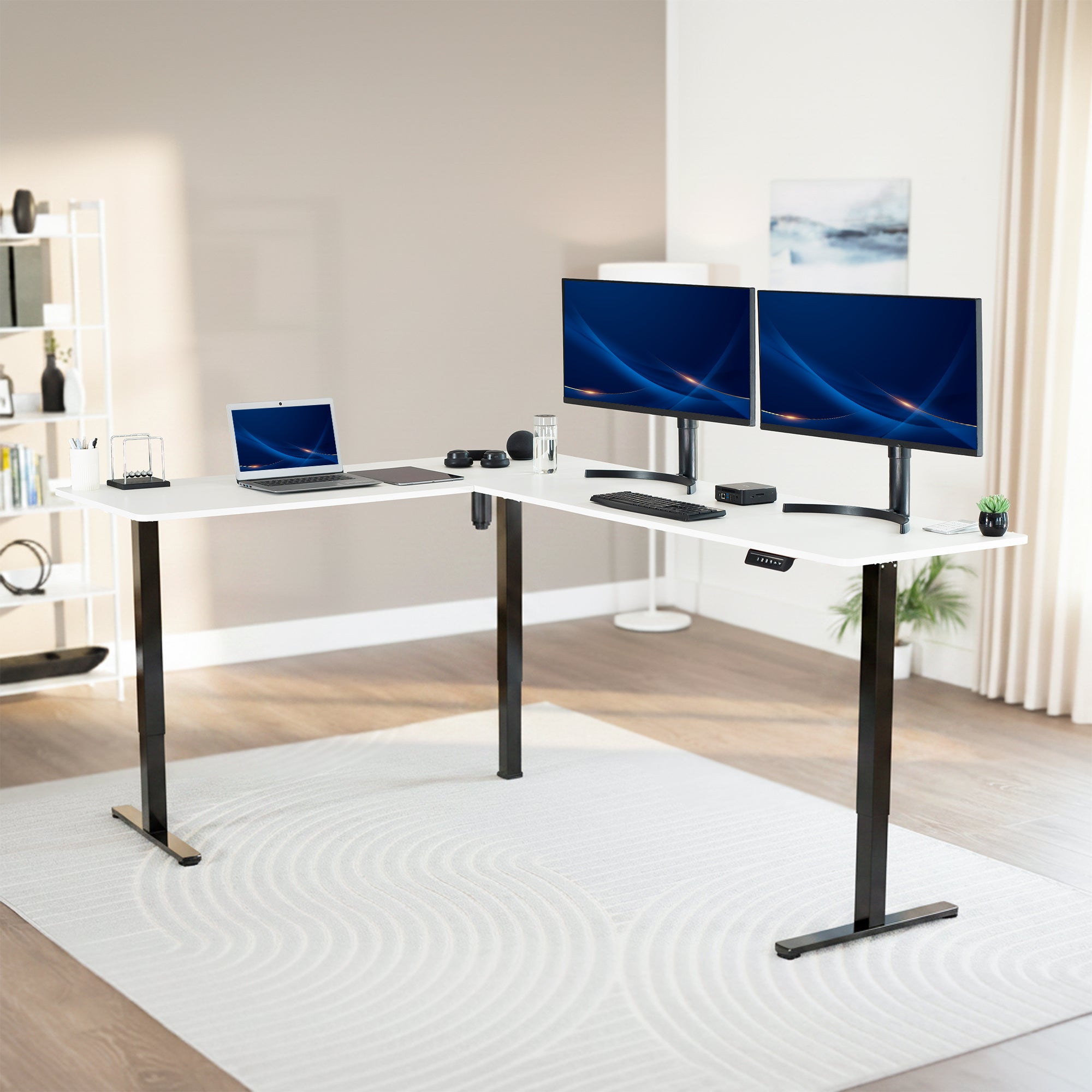 Modern office setup with a standing l-shaped desk, laptop, and two monitors in a bright room.