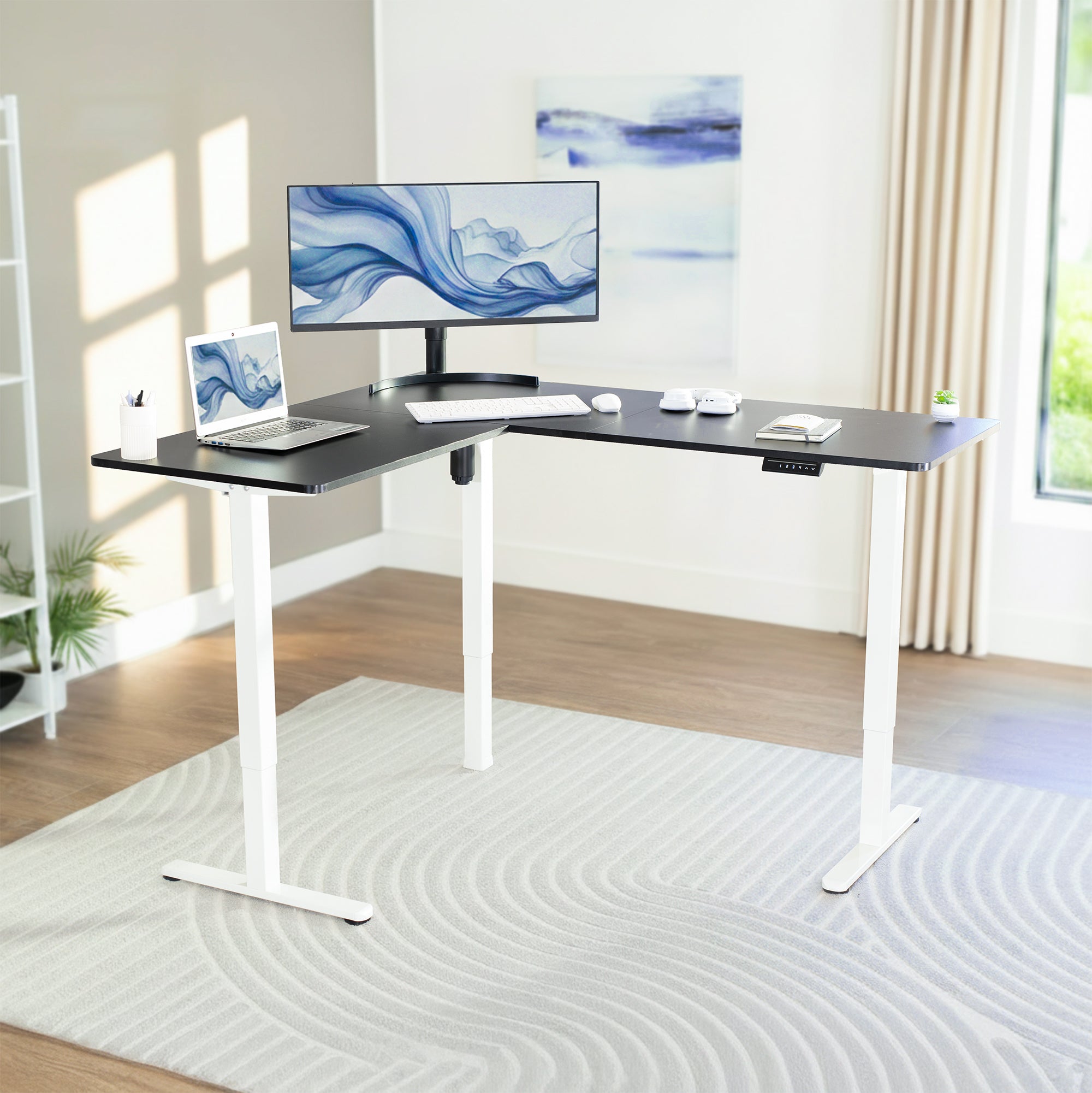 Modern office setup with a adjustable desk, computer monitor, and laptop in a bright room.