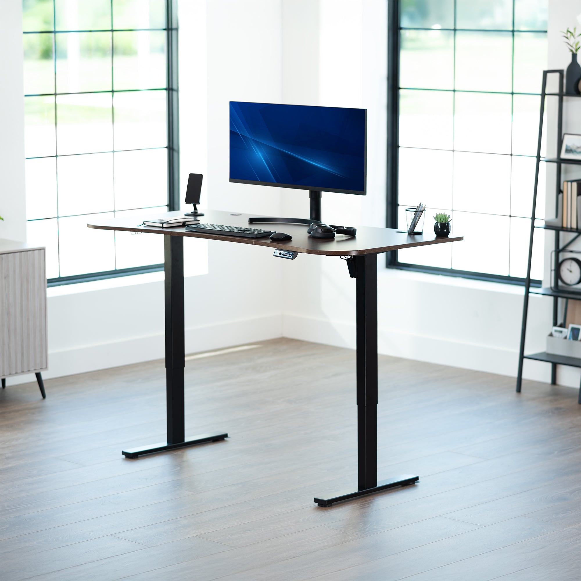 Dark walnut, electric, sit to stand, height adjustable desk in office setting.