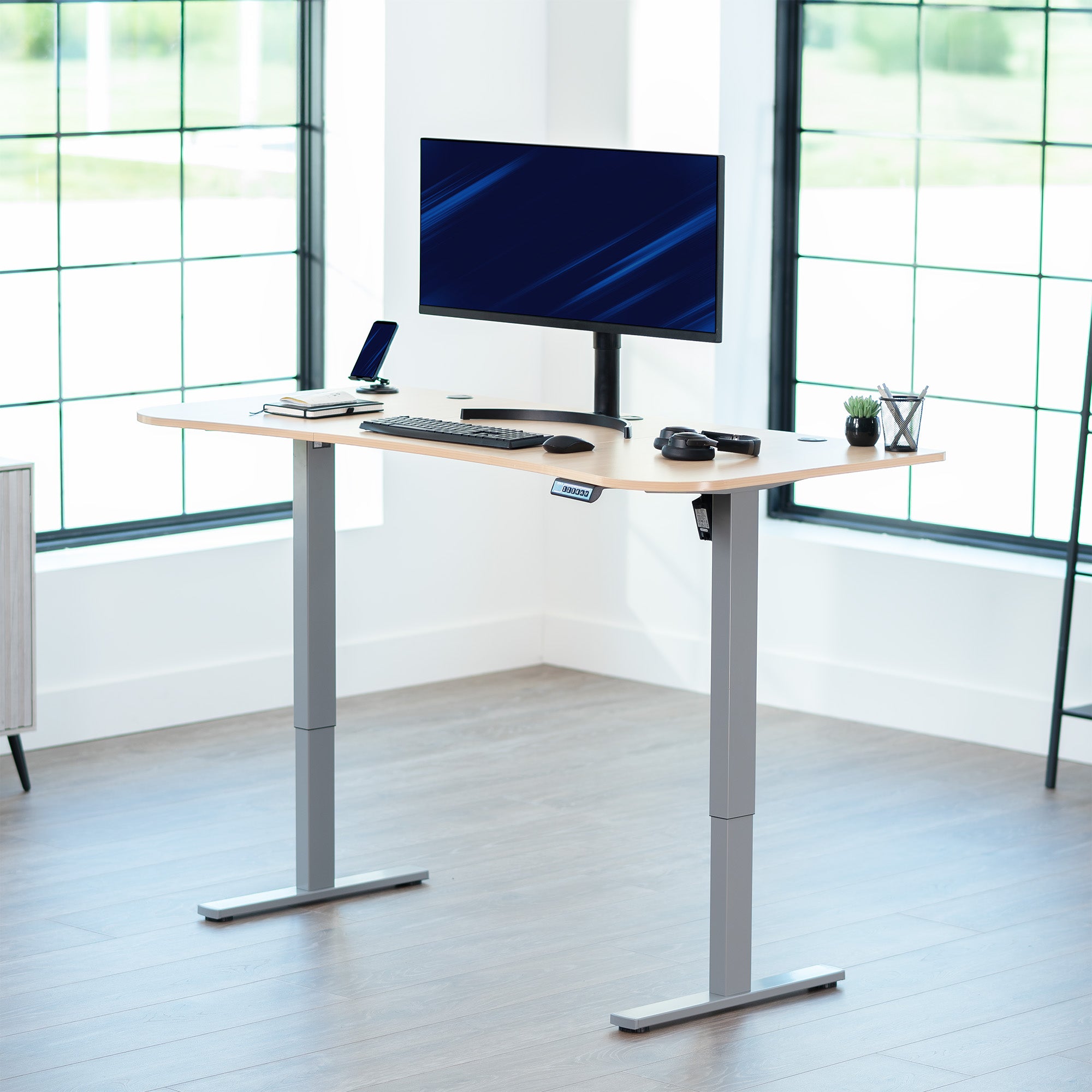 Light wood top grey frame, electric, sit to stand, height adjustable desk in office setting.