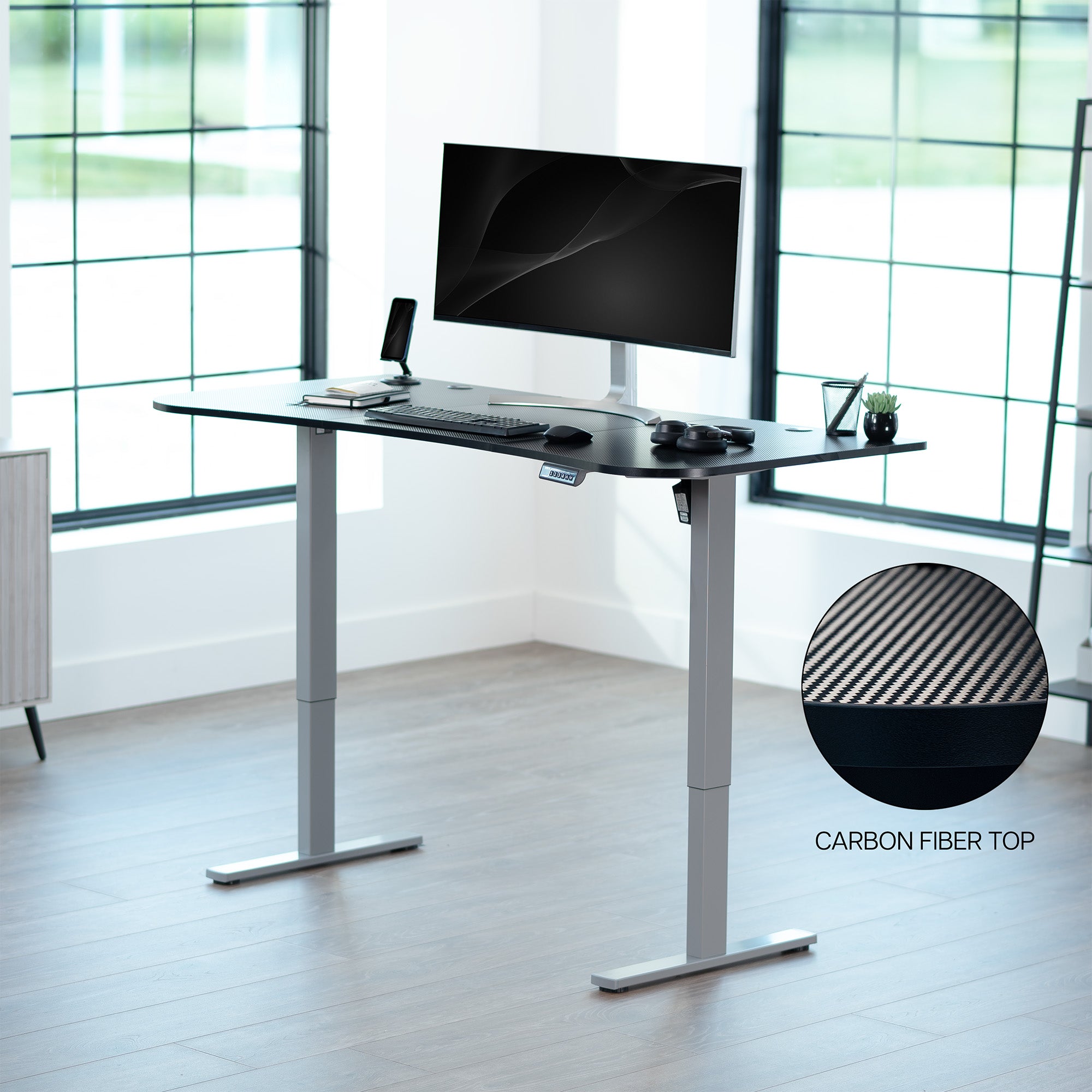 Carbon fiber top grey frame, electric, sit to stand, height adjustable desk in office setting.