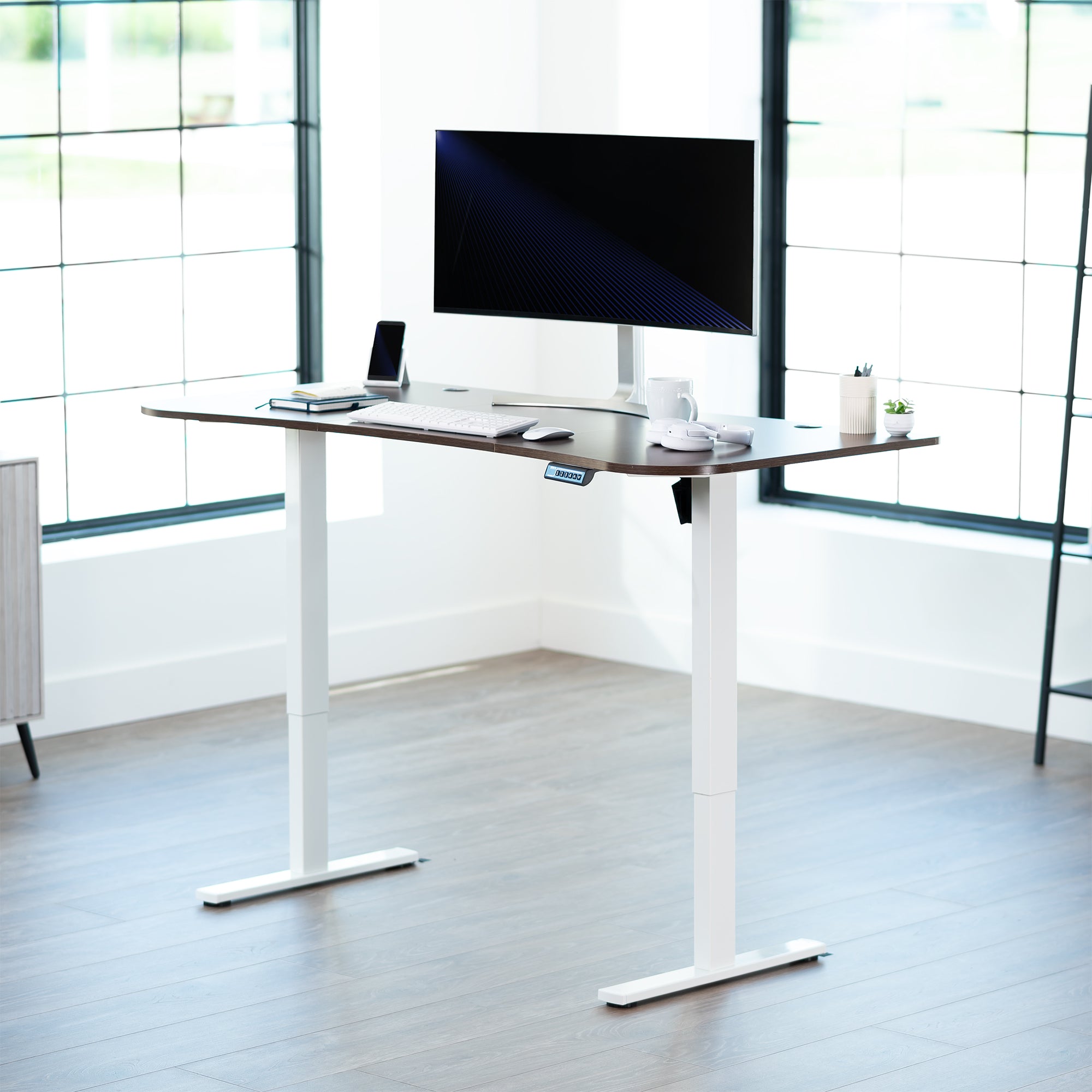 Dark walnut top white frame, electric, sit to stand, height adjustable desk in office setting.