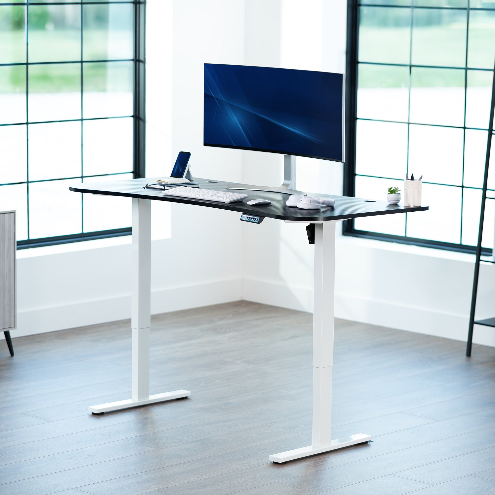 Carbon fiber top white frame, electric, sit to stand, height adjustable desk in office setting.