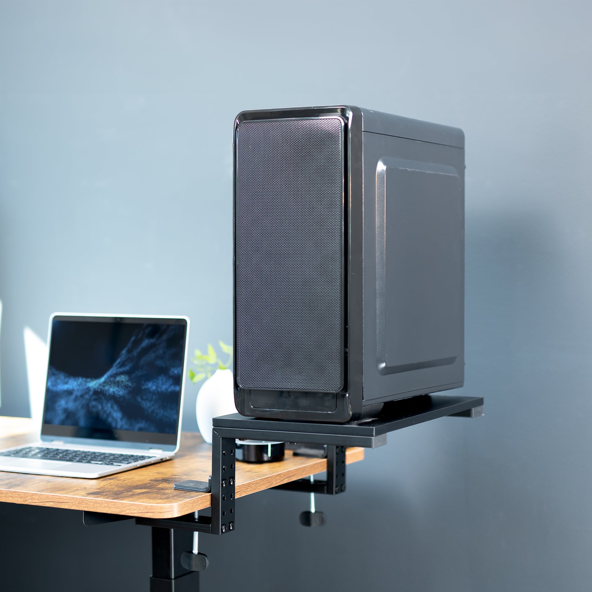 Black computer tower on a desk with a laptop and plant against a gray wall