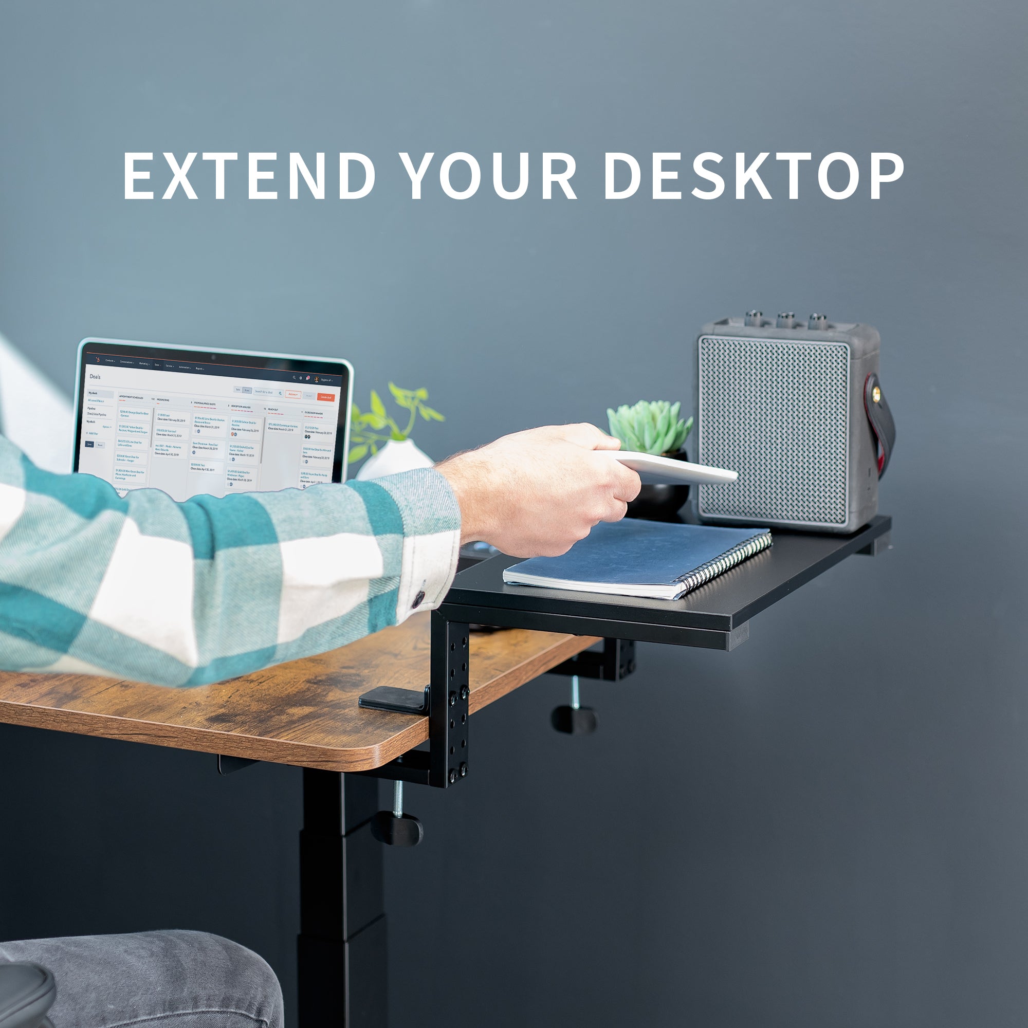Person using a desk extension with a laptop and notebook on a dark gray background