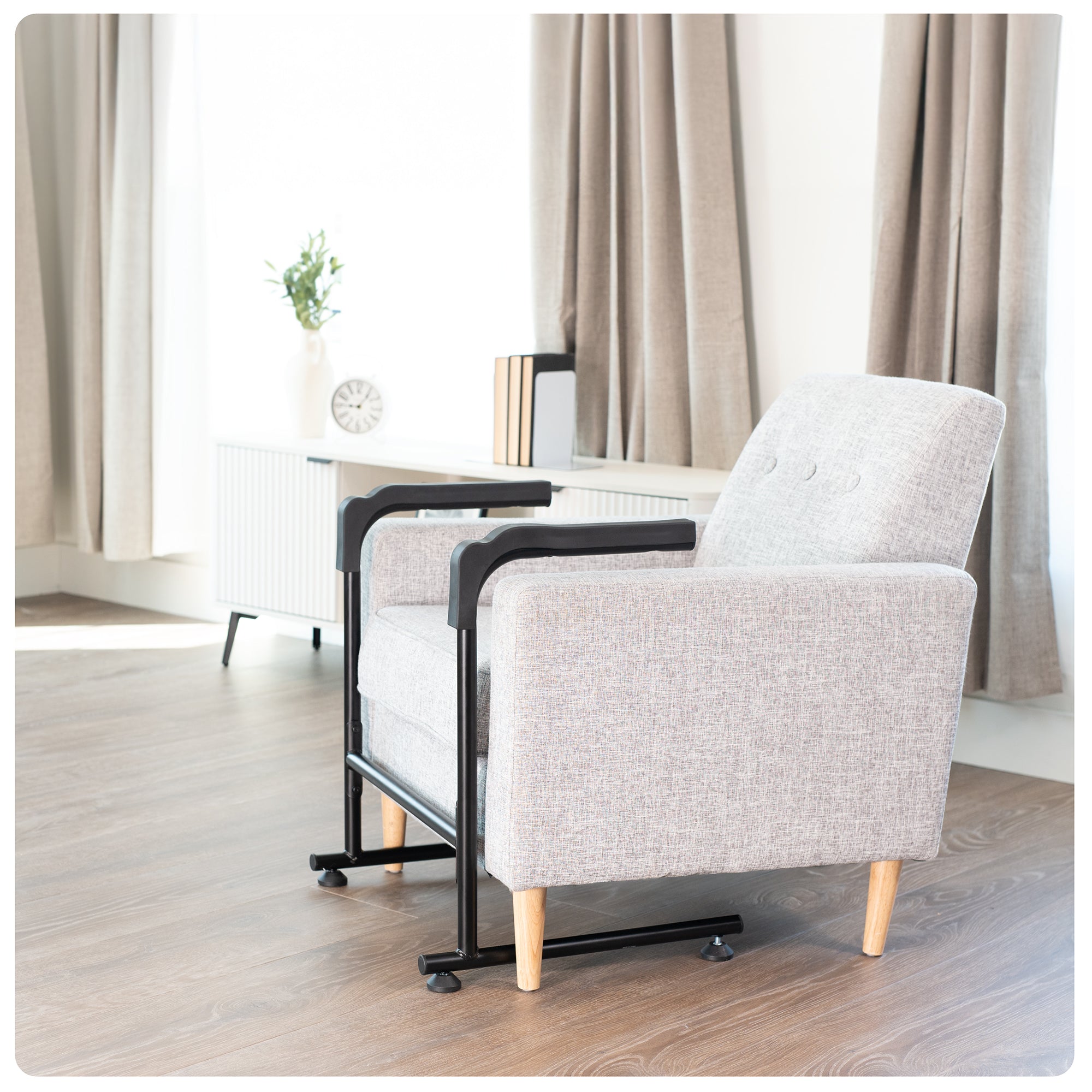 Gray armchair with black metal stand assist frame in a room with curtains and a clock.