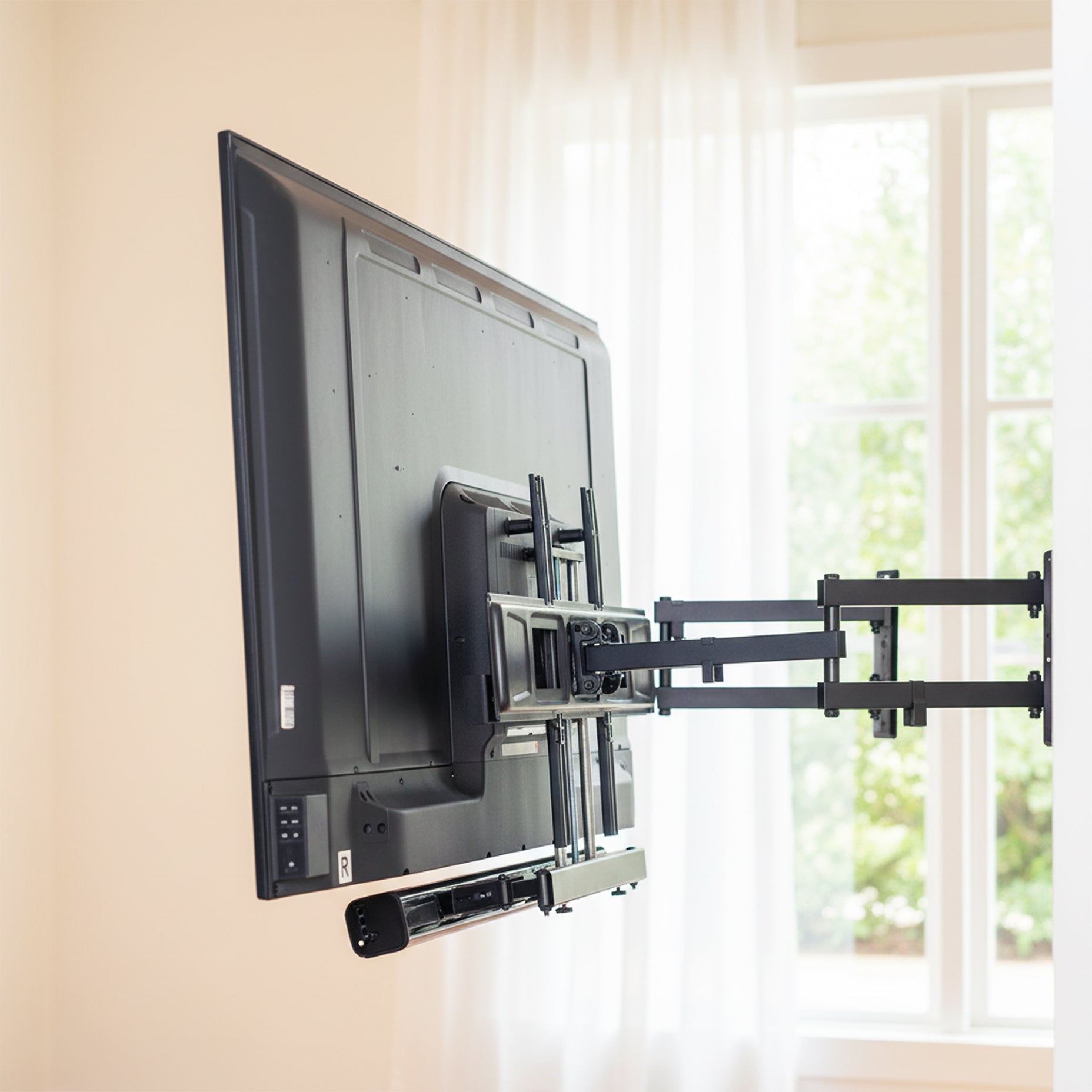 TV mounted on a wall with a bracket in a room with a window featuring a Soundbar TV Mount