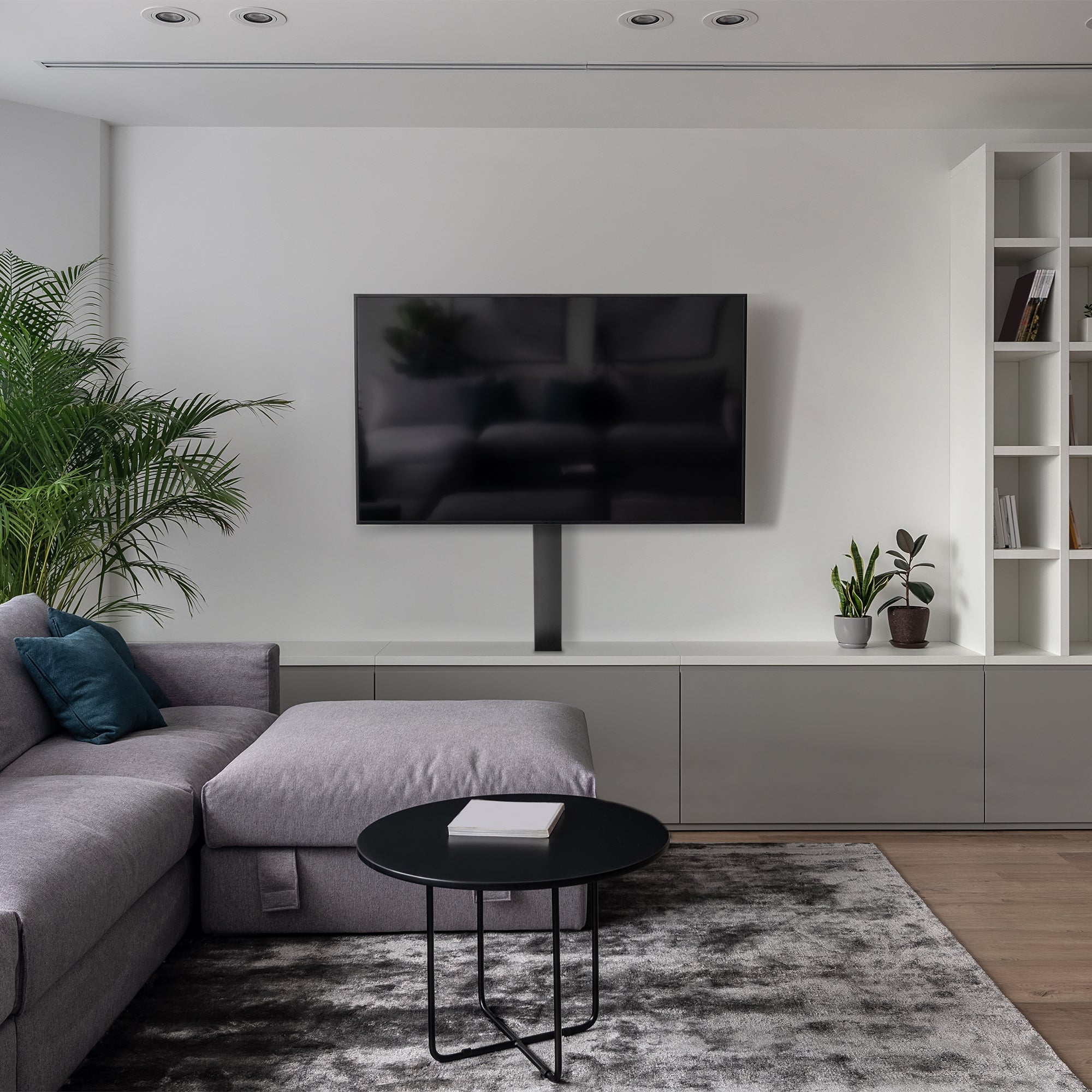 Modern living room with a gray sectional sofa, round black coffee table, and wall-mounted TV.