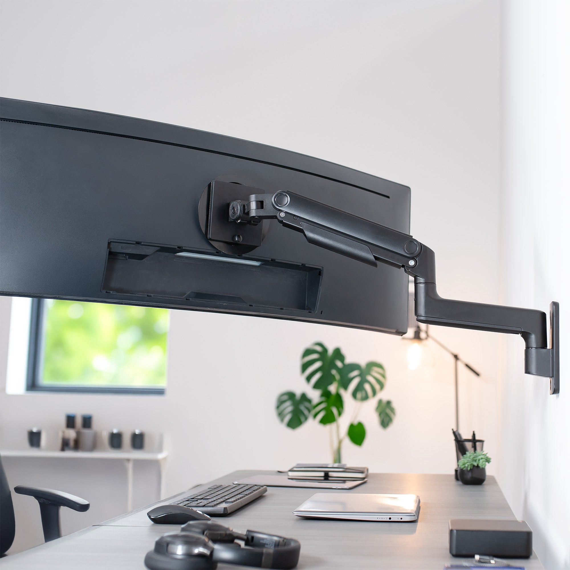 A single ultrawide computer monitor attached to a pneumatic arm wall mount in an office setting.