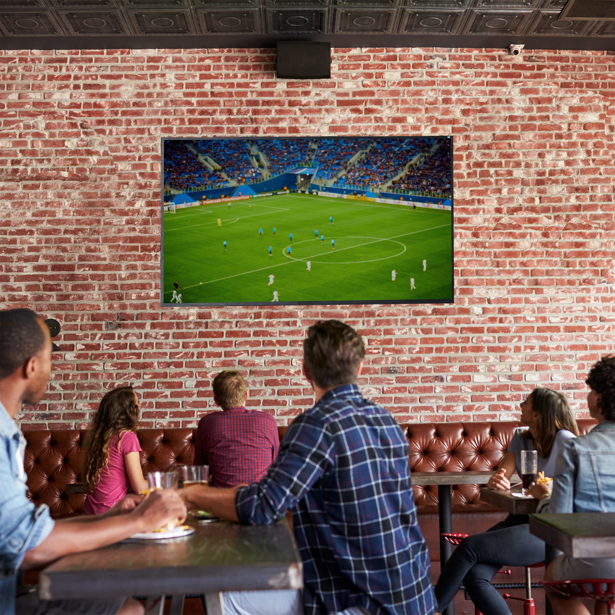 A black VESA wall mount with a TV on it in a restaurant setting with a game on the screen.
