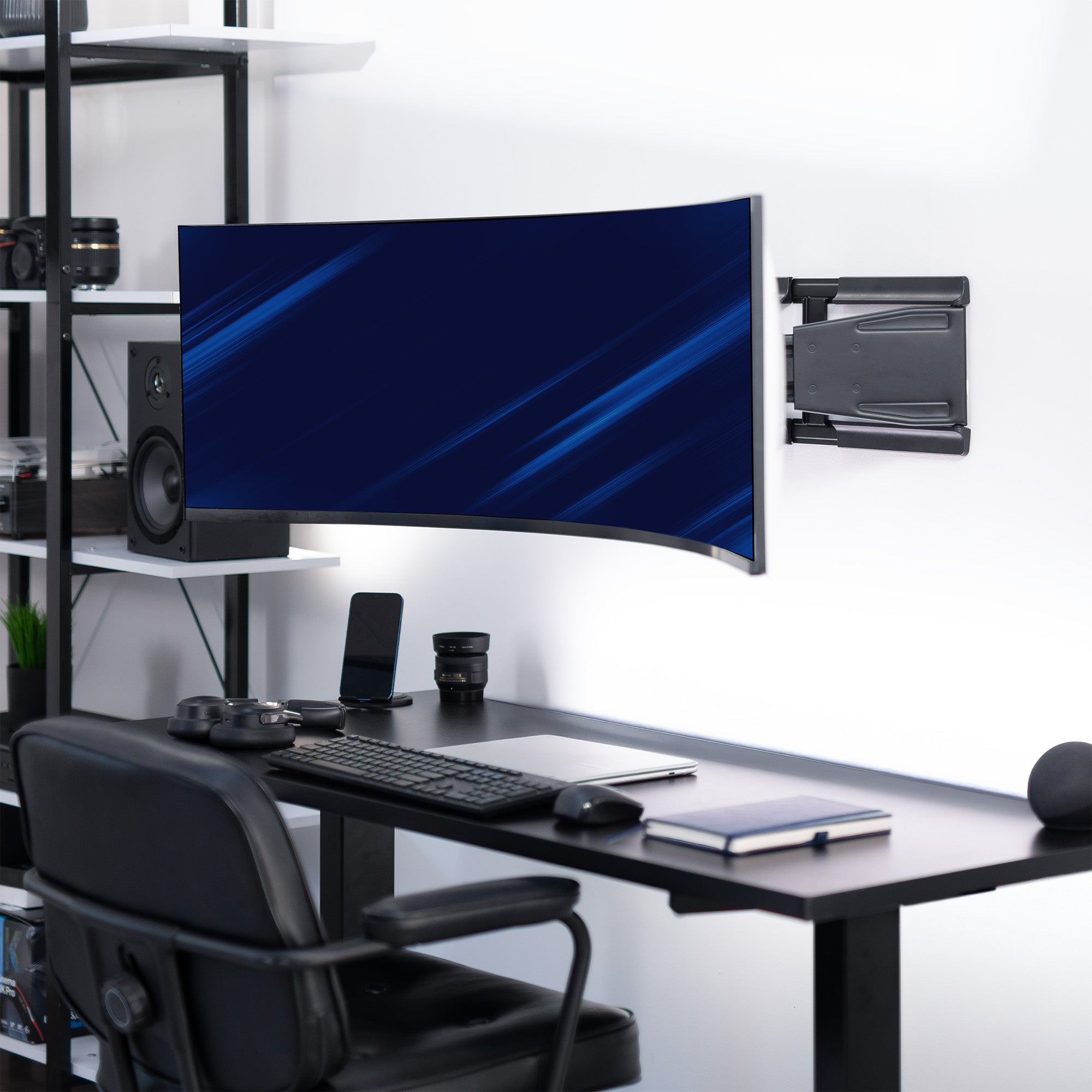 Modern office setup with a large curved monitor wall mounted, a desk, chair, and shelves.