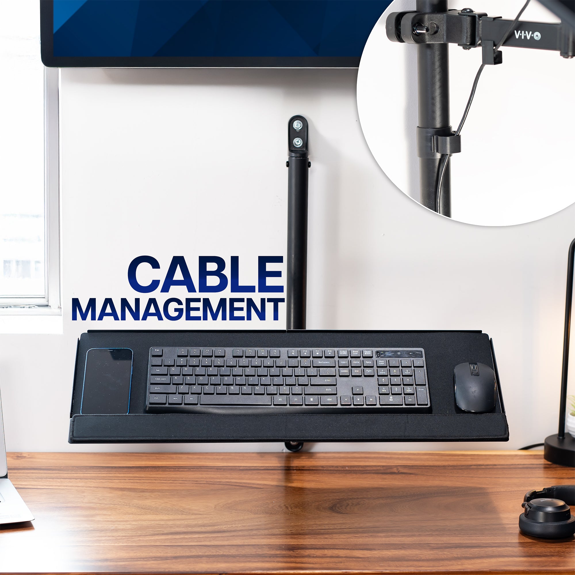 Desk setup with keyboard on wall-mounted keyboard tray and a wall-mounted monitor on a wooden desk with cable management solution.
