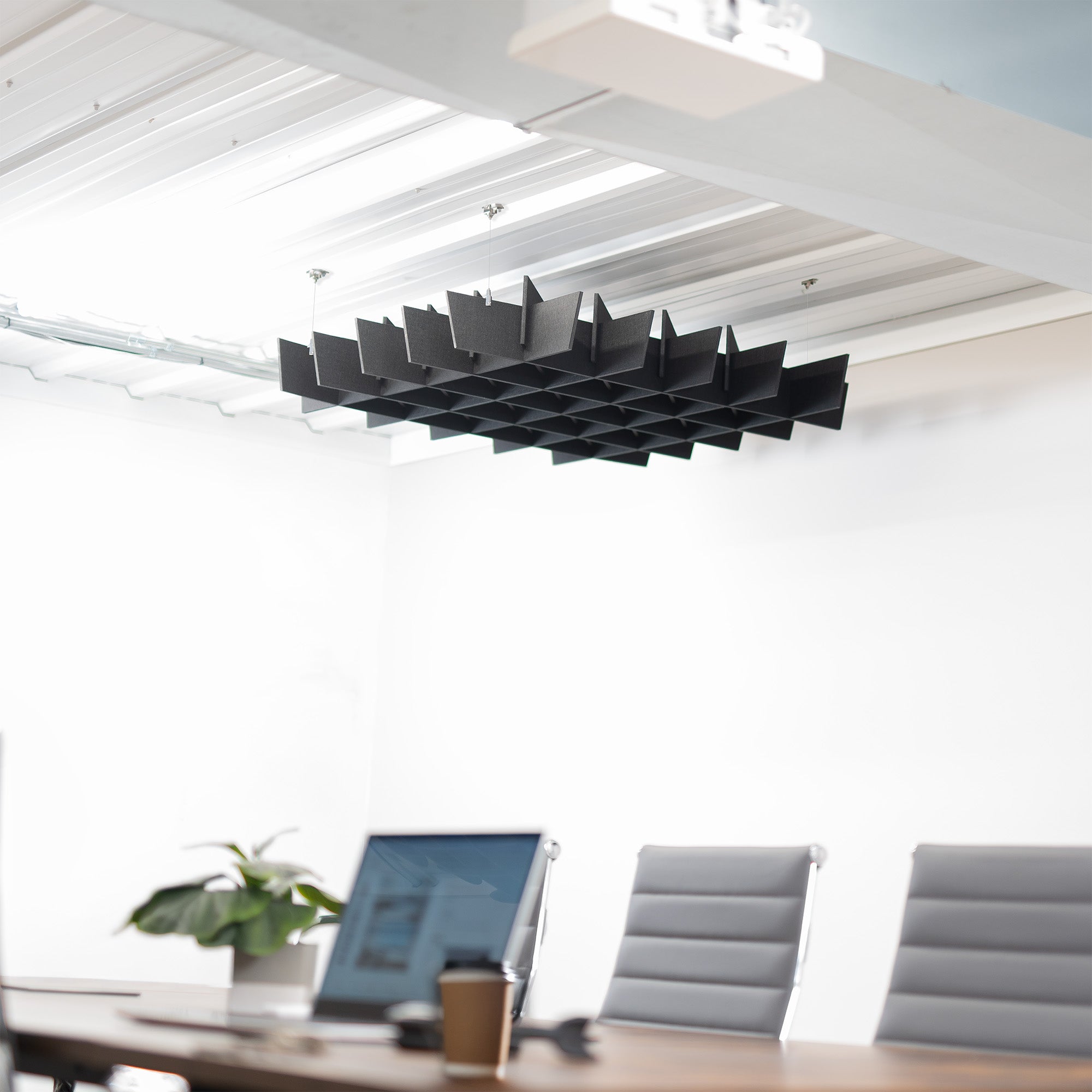 A black acoustic dual-layer ceiling waffle panel with a geometric pattern, mounted on a ceiling in a conference room.