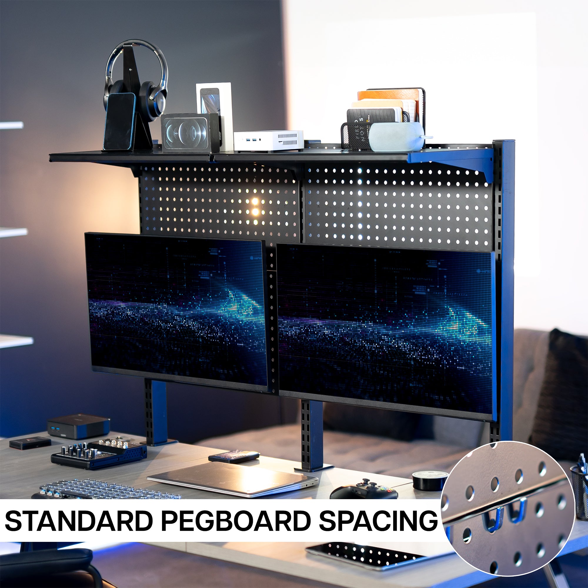 A black clamp-on pegboard monitor mount with a shelf, holding two flat-screen monitors, a speaker, and various desk accessories.