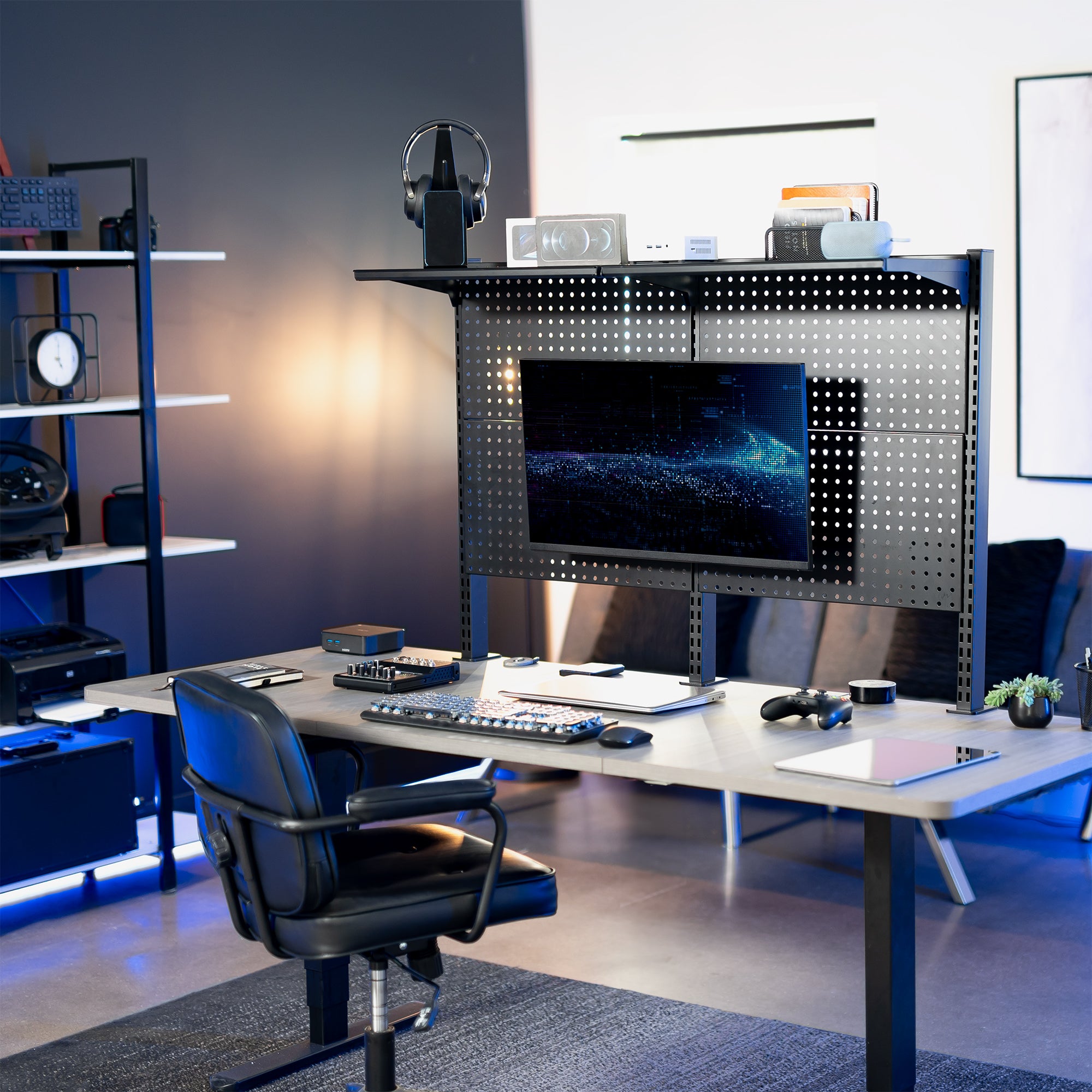 A black clamp-on pegboard monitor mount with a shelf, holding a flat-screen monitor, a speaker, and various desk accessories.