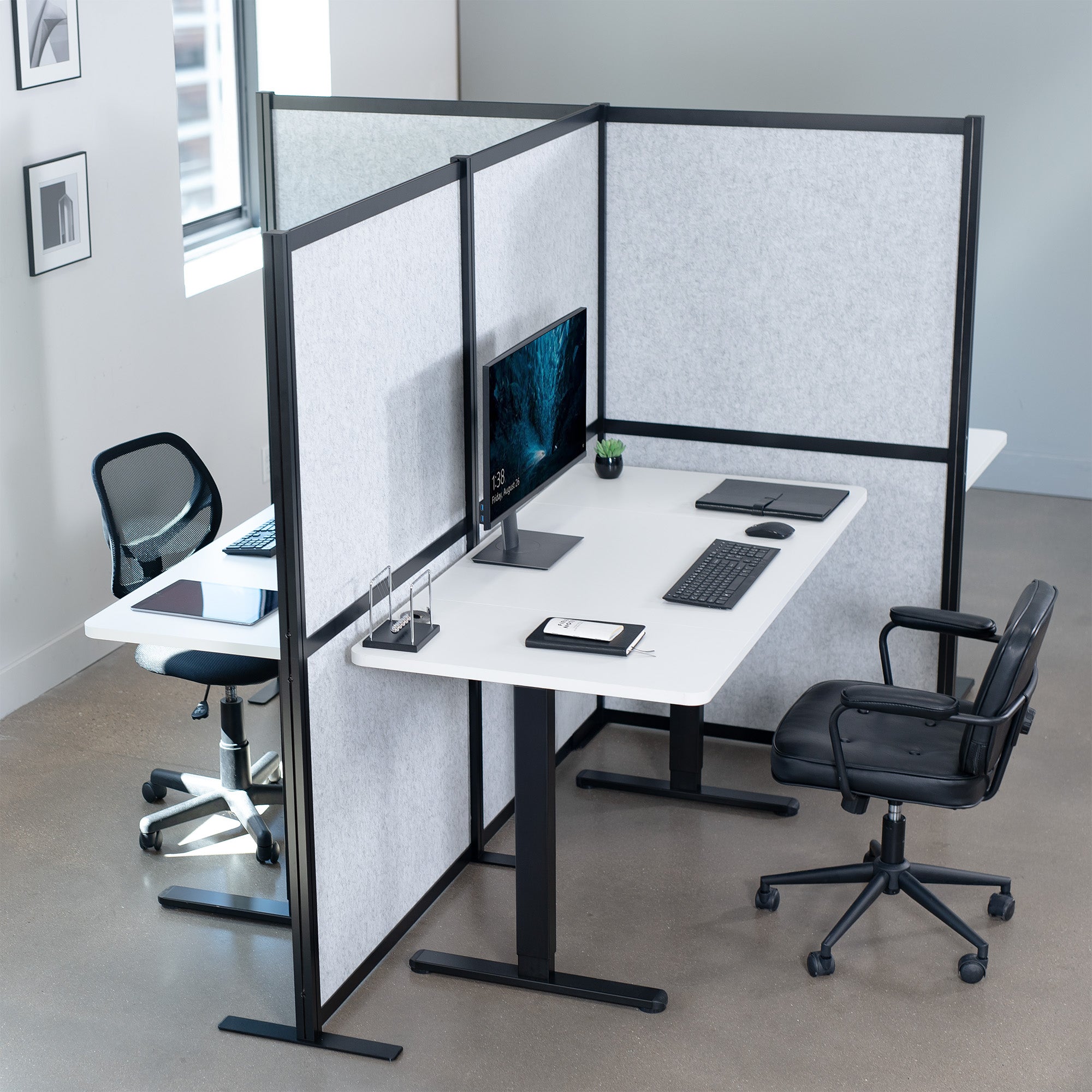 Modern office setup with desks divided by a freestanding privacy partition in a room with large windows.