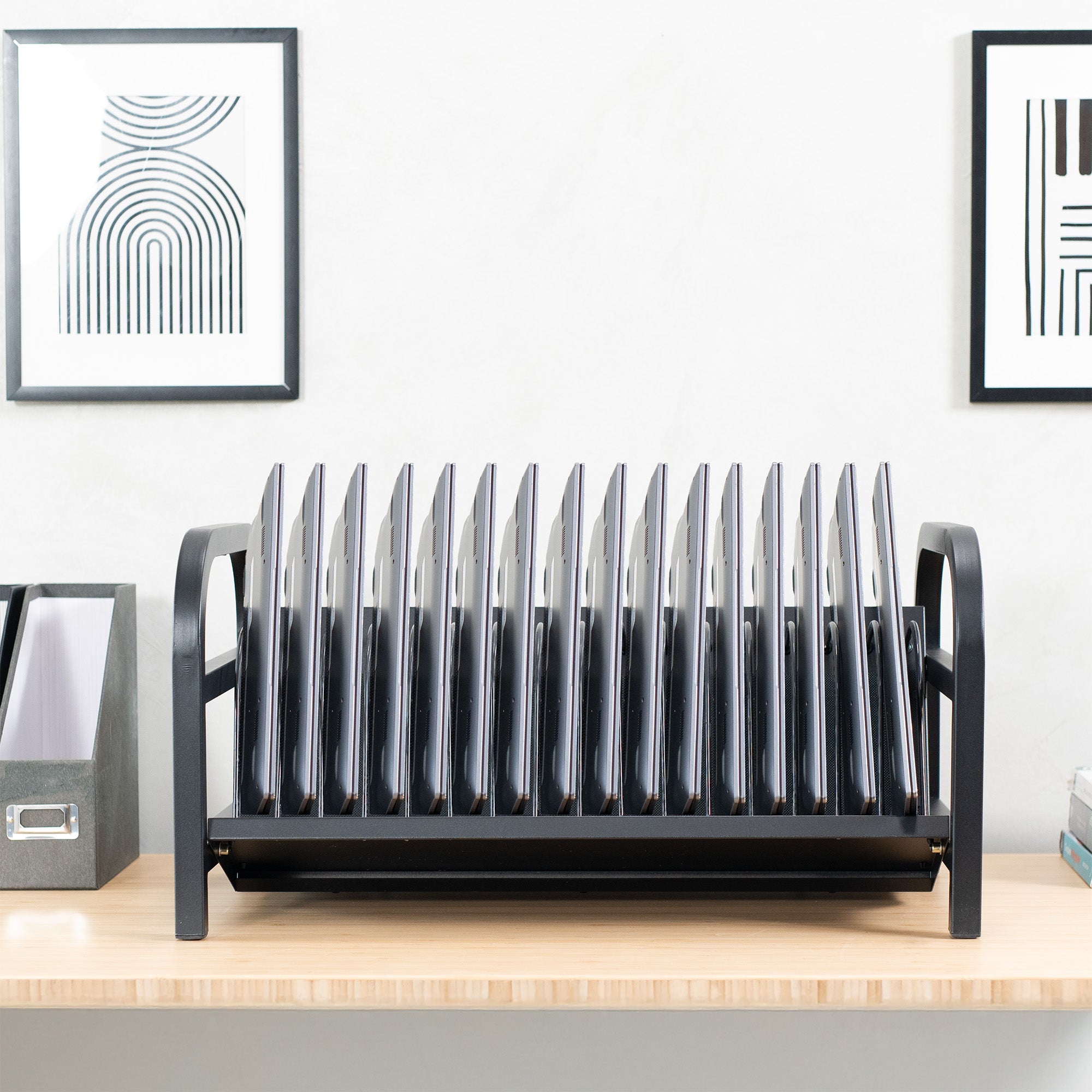 Black device charging rack on a wooden surface with two framed artworks in the background.