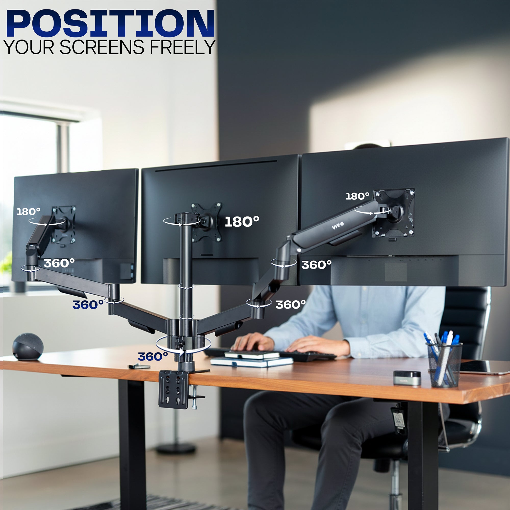 Person using a computer setup with three monitors on a desk, featuring a monitor stand with 'Position Your Screens Freely' text.