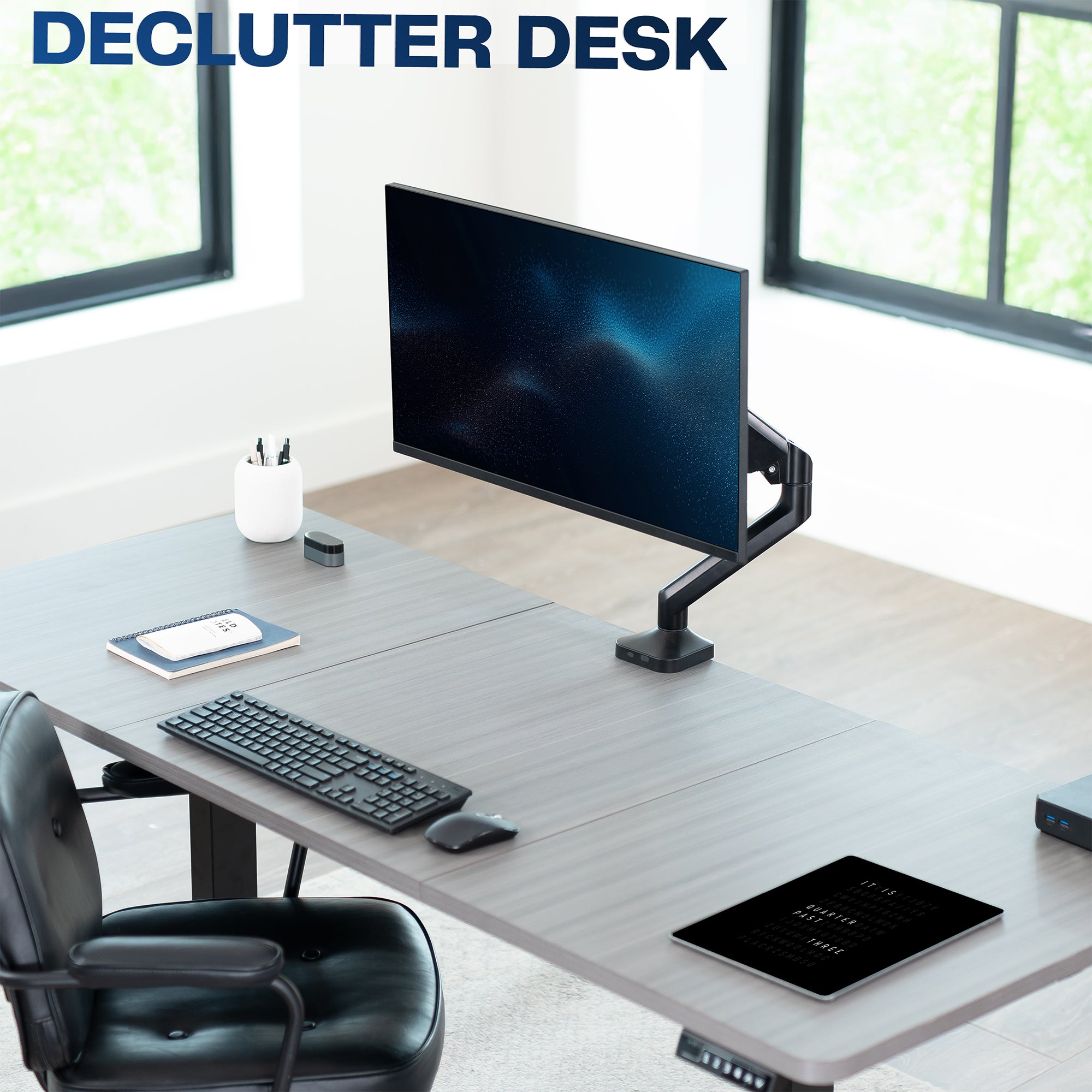 Modern office desk setup with computer monitor, keyboard, and chair in a bright room.