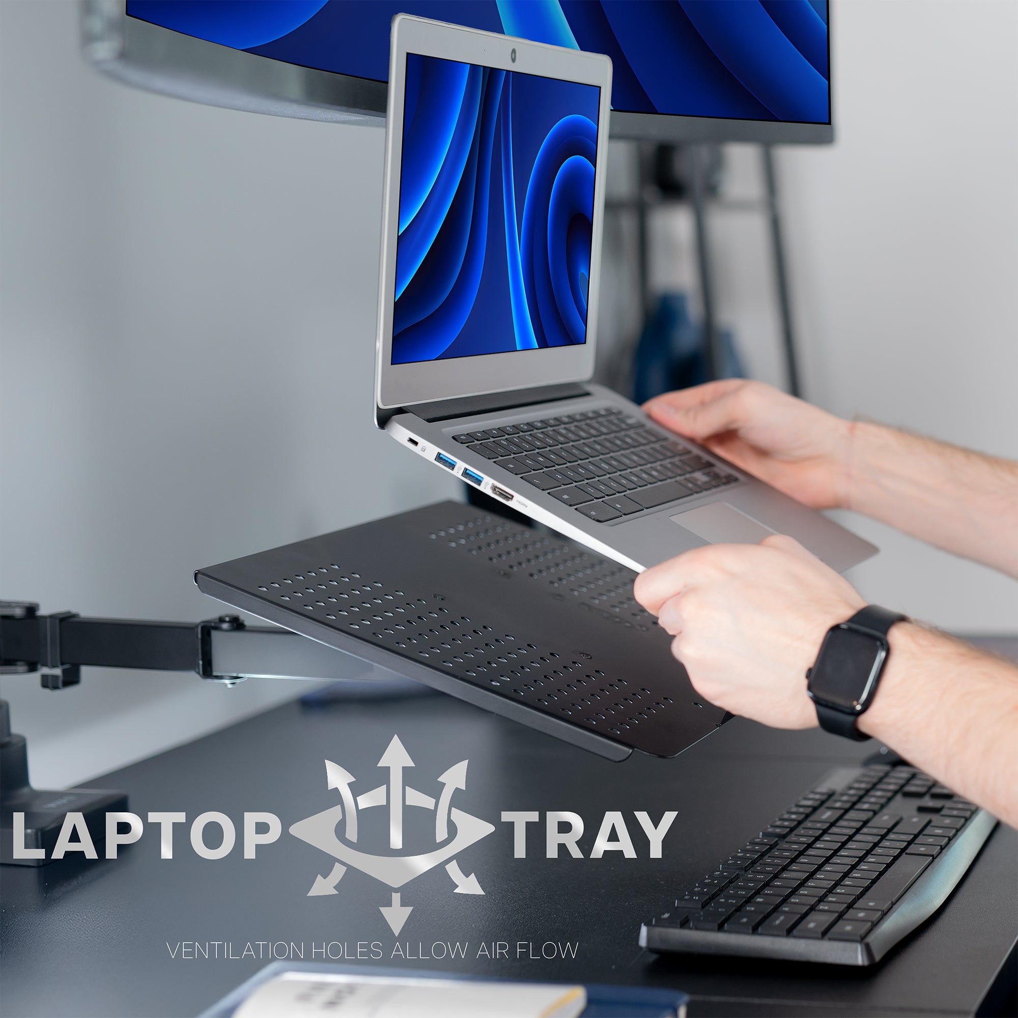 Person using a laptop on a laptop tray with ultrawide monitor in the background. Laptop tray has ventilation holes to allow air flow.