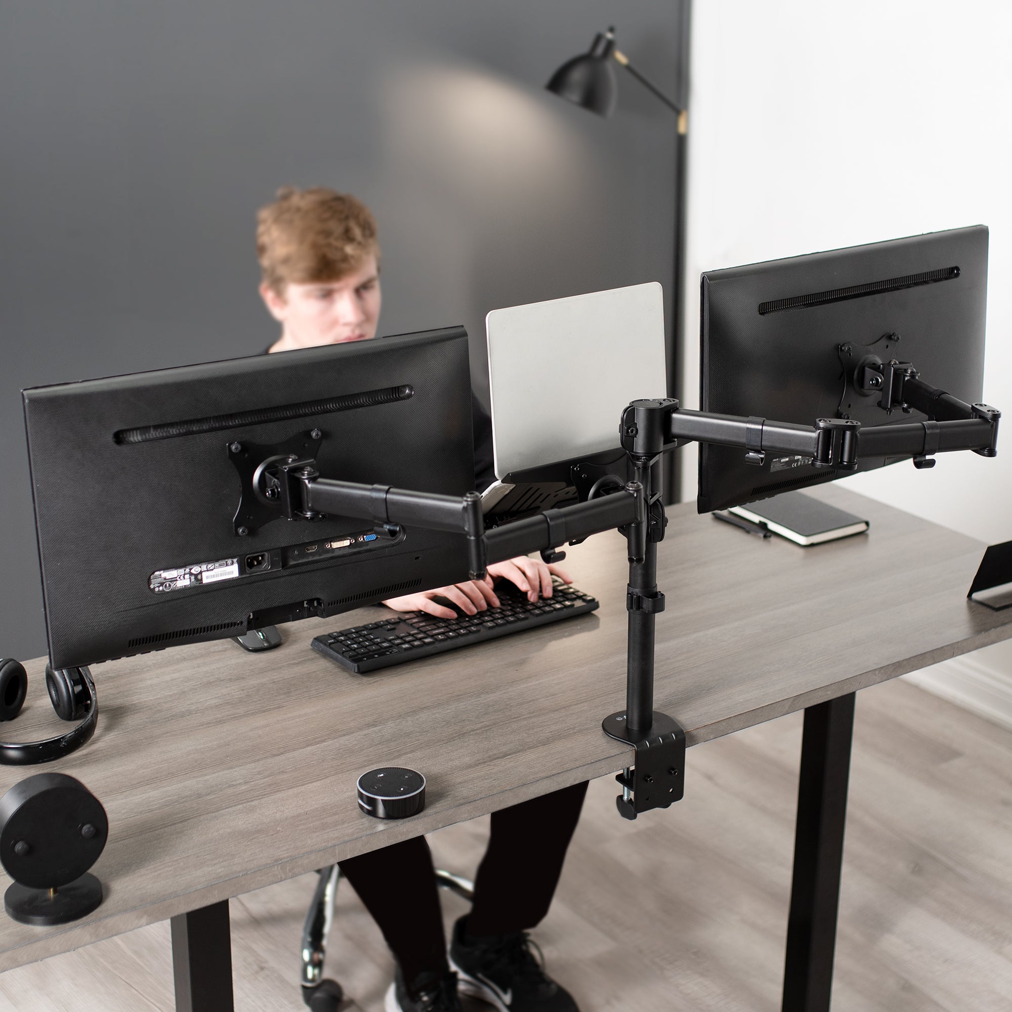 A black desk mount that can hold two monitors and one laptop.