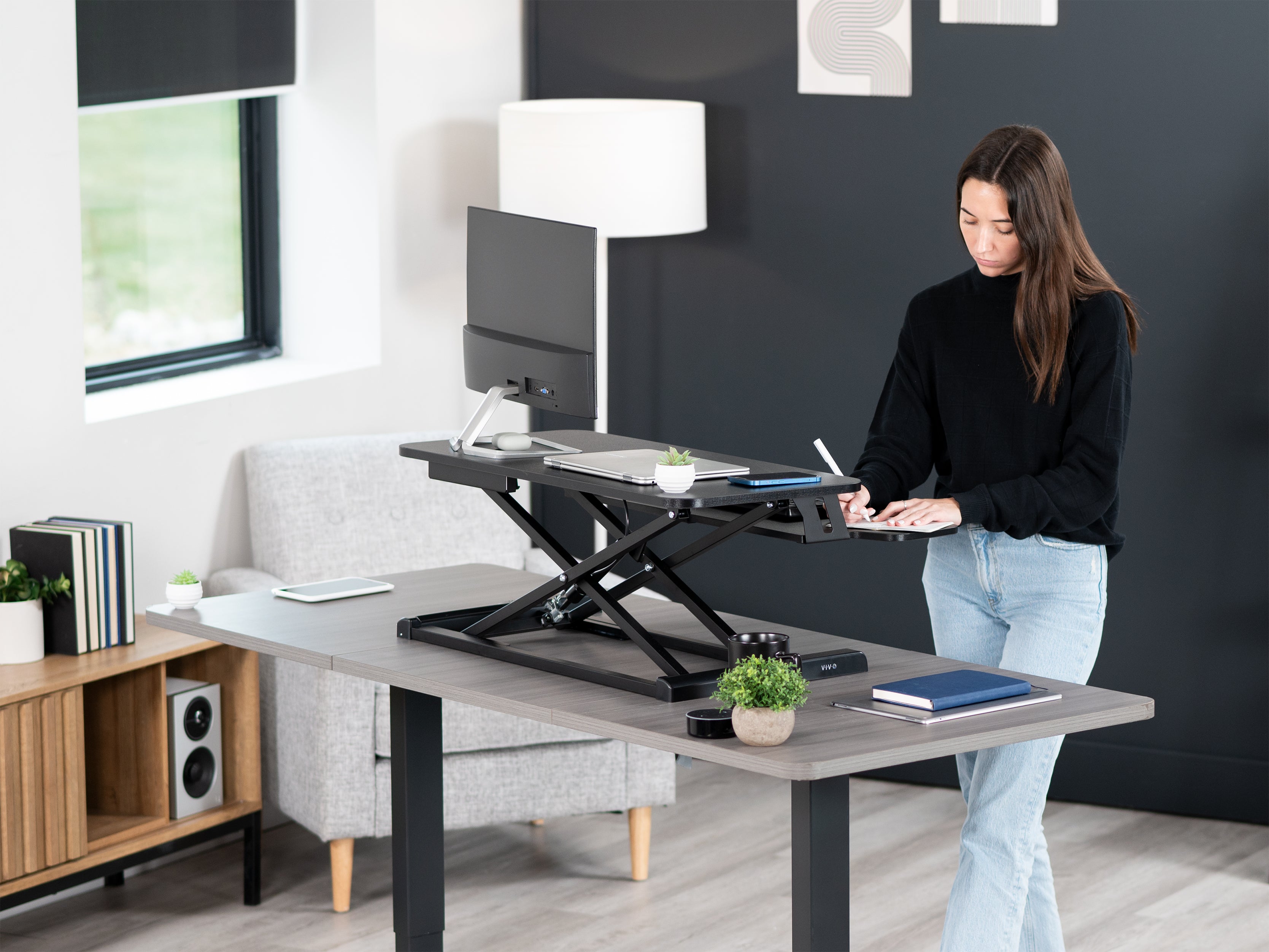 model standing at desk writing in a notebook in a home office setting. 