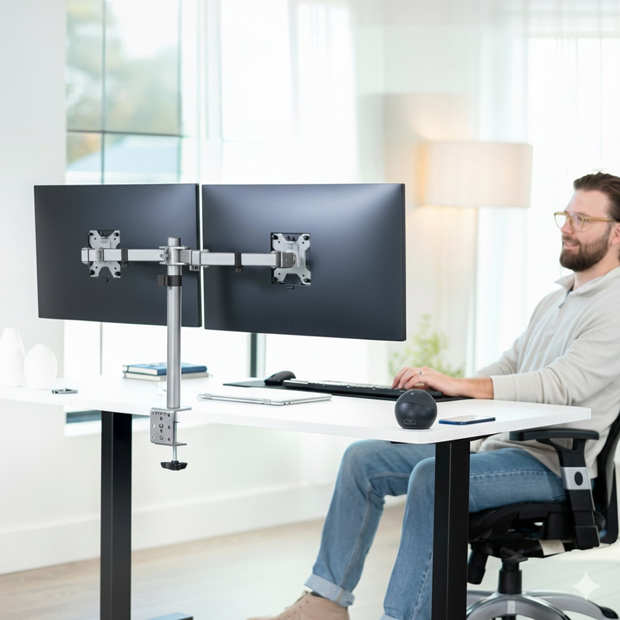 Person using a dual monitor stand at a desk in a bright room.