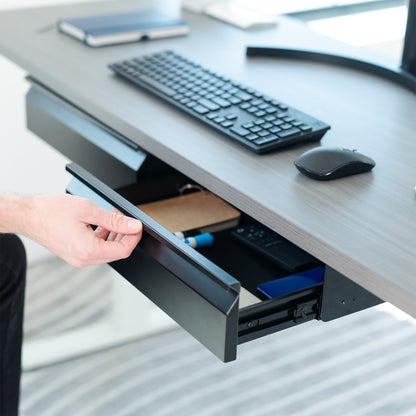 Person opening a desk drawer with office supplies on a desk.
