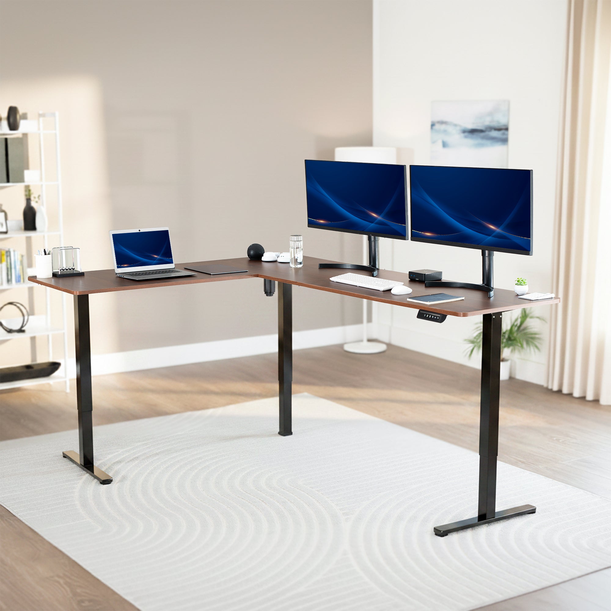 Modern office setup with a standing l-shaped desk, laptop, and two monitors in a bright room.