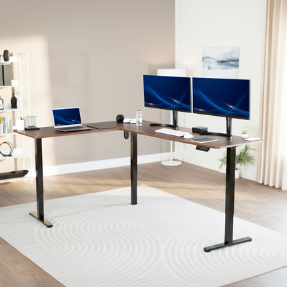 Modern office setup with a standing l-shaped desk, laptop, and two monitors in a bright room.