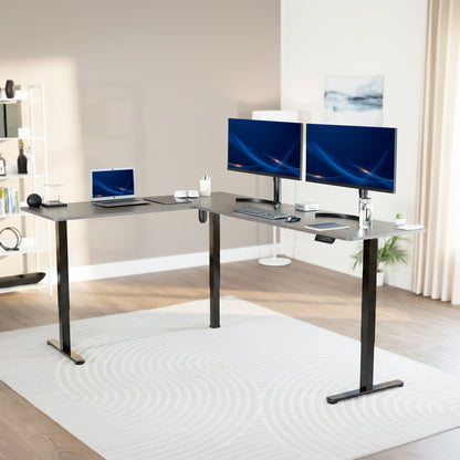 Modern office setup with a standing l-shaped desk, laptop, and two monitors in a bright room.