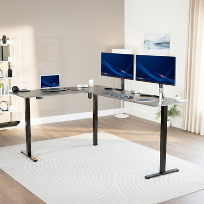 Modern office setup with a standing l-shaped desk, laptop, and two monitors in a bright room.