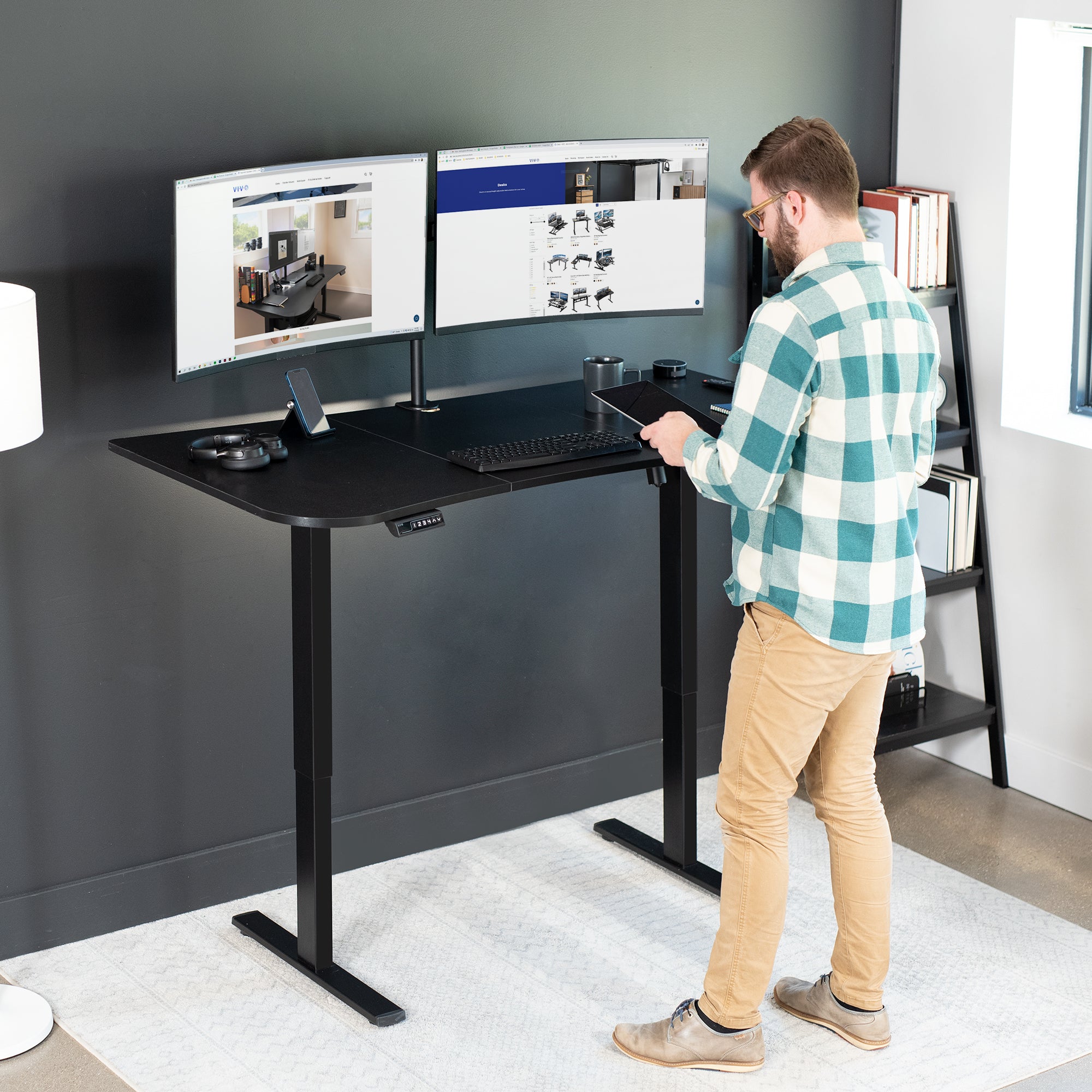 A man working at a standing height adjustable desk in a modern office workspace.