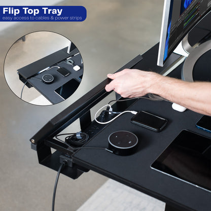 Desk with flip top tray for cable management and power strips, showing a hand plugging in devices.