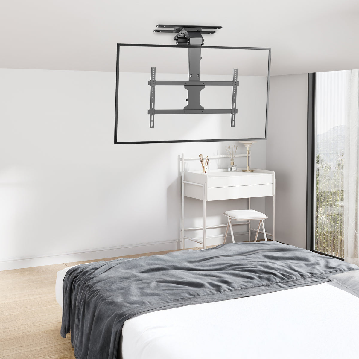 A ceiling-mounted TV bracket suspended from the ceiling in a modern bedroom, shown holding a large framed television above a bed and vanity desk.