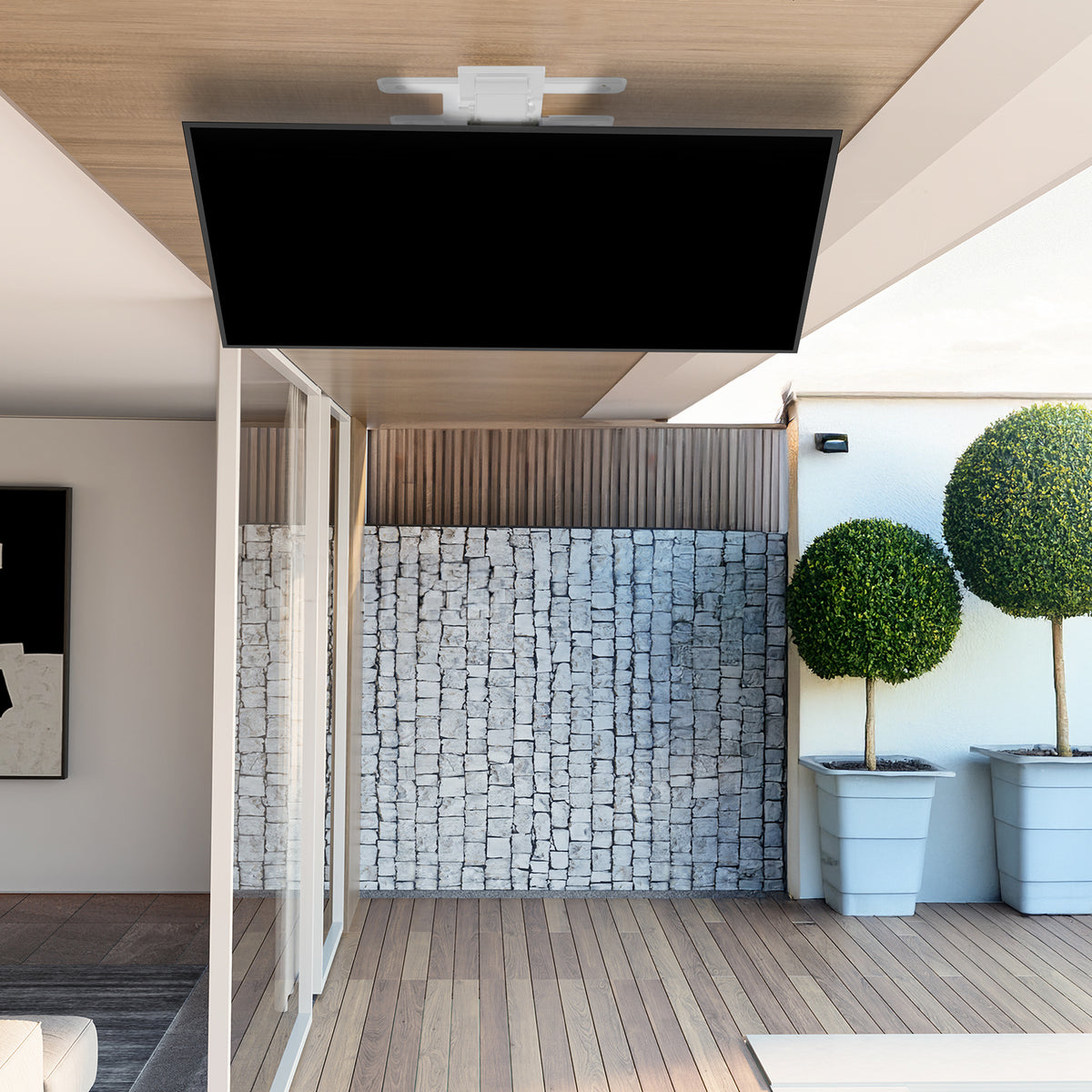 A ceiling-mounted flat-screen TV on an electric swivel bTV mount in a modern living room setting. The TV displays a landscape image, while the bracket is visible behind the screen.