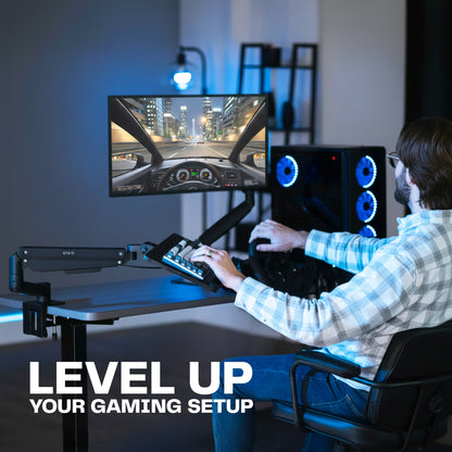 Person playing a racing game on a computer setup with a monitor on a desk mount and a keyboard tray clamped onto their desk, seated in a gaming chair creating the ultimate gaming setup.