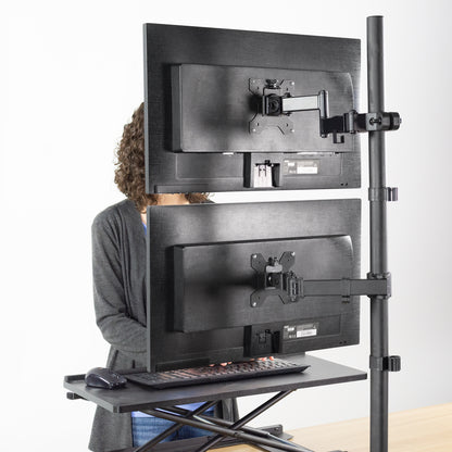 Person using a standing desk with dual monitor setup on a white background showing a Pole Mount VESA Monitor Arm - 17" to 32" Screens on the pole