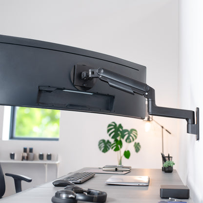 A single ultrawide computer monitor attached to a pneumatic arm wall mount in an office setting. 
