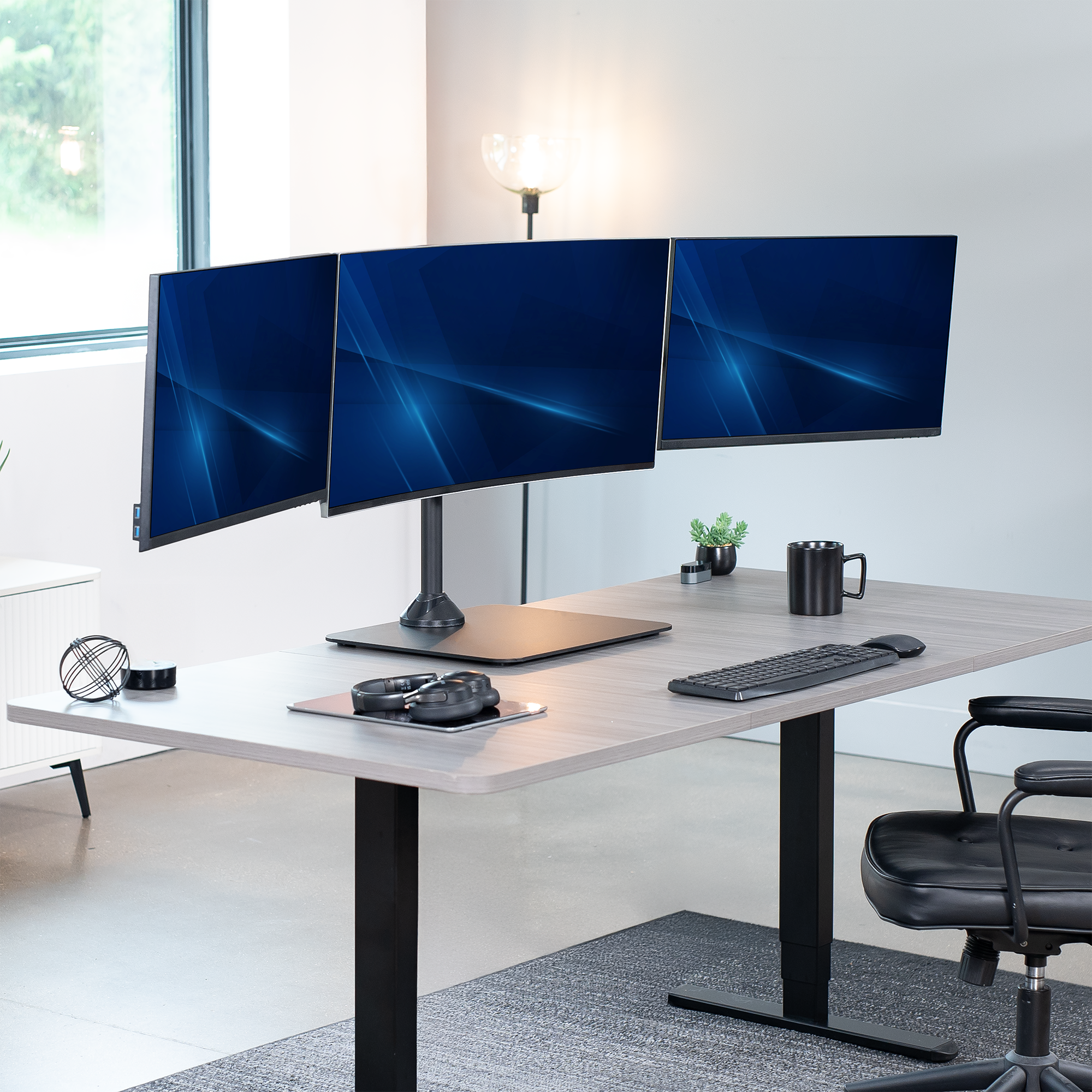 Modern office desk setup with three monitors, keyboard, and mouse.