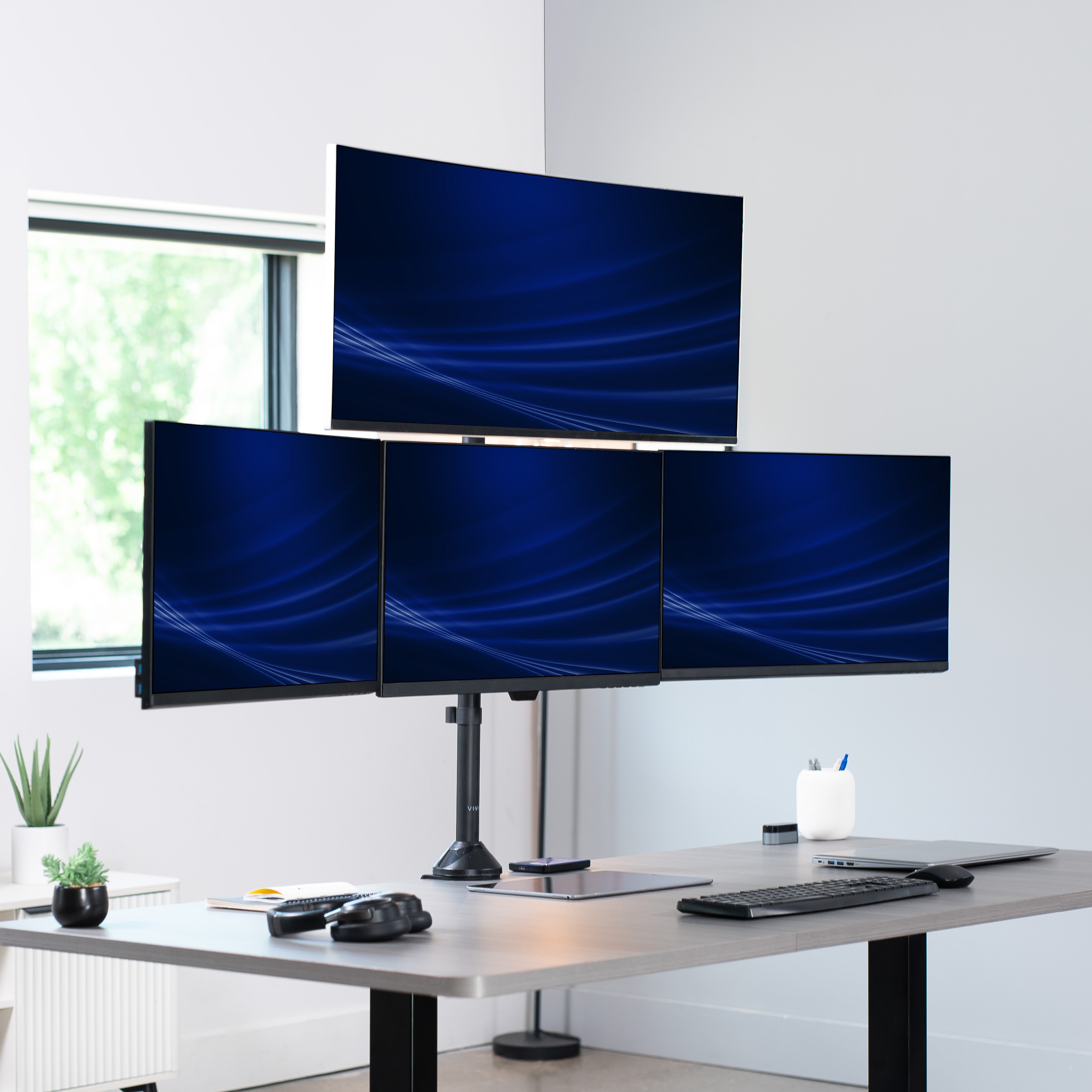Four computer monitors on a desk with a modern office setting