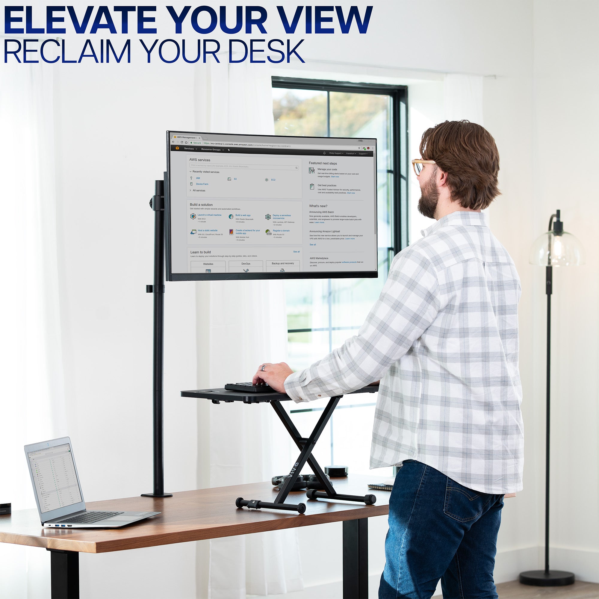 Man using a standing keyboard desk riser and extra tall monitor stand in a home office setting with text 'Elevate Your View, Reclaim Your Desk'.