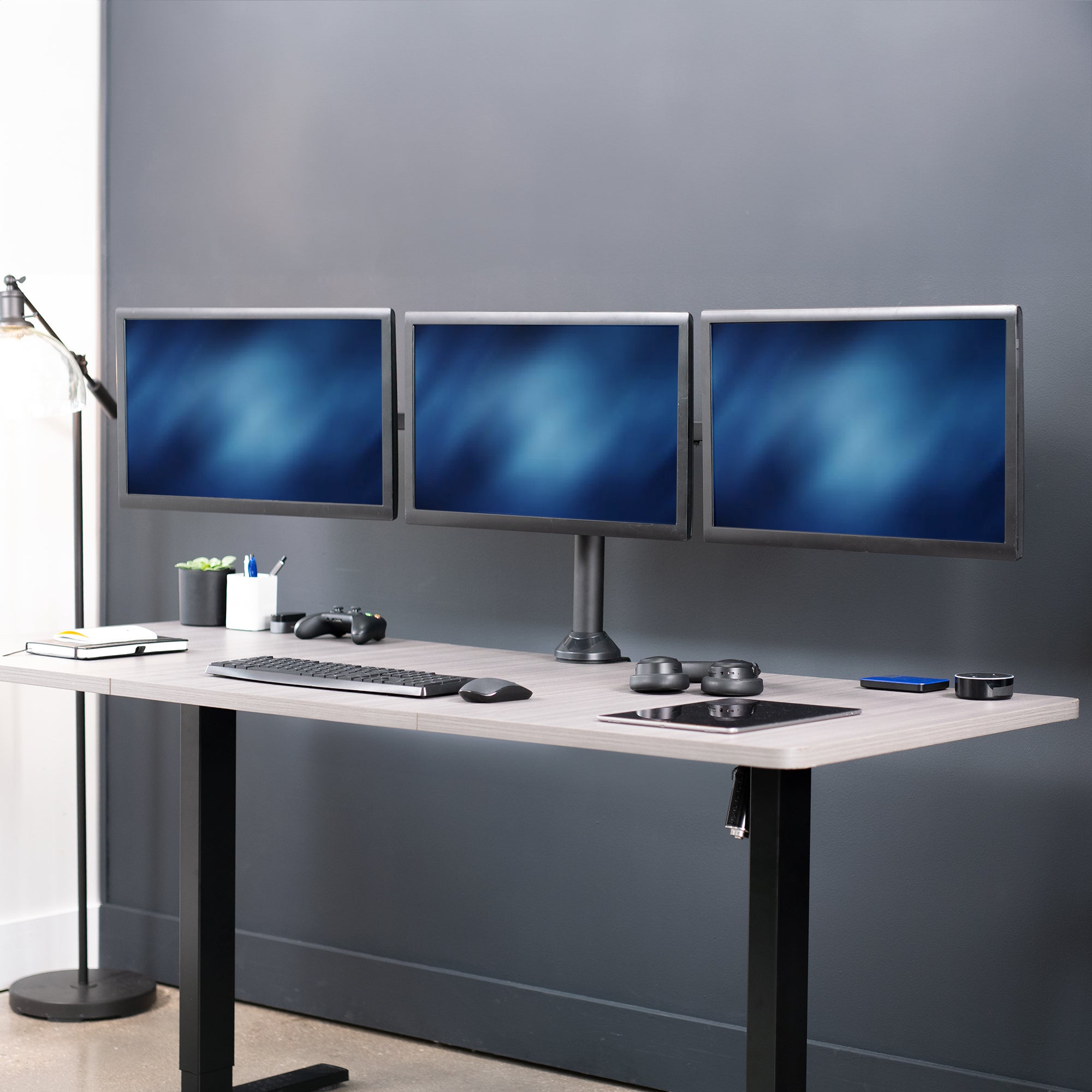Modern office setup with a standing desk and three monitors on a gray wall.