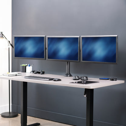 Modern office setup with a standing desk and three monitors on a gray wall.