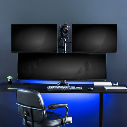 Modern gaming desk setup with dual monitors and gaming chair in a dark room.