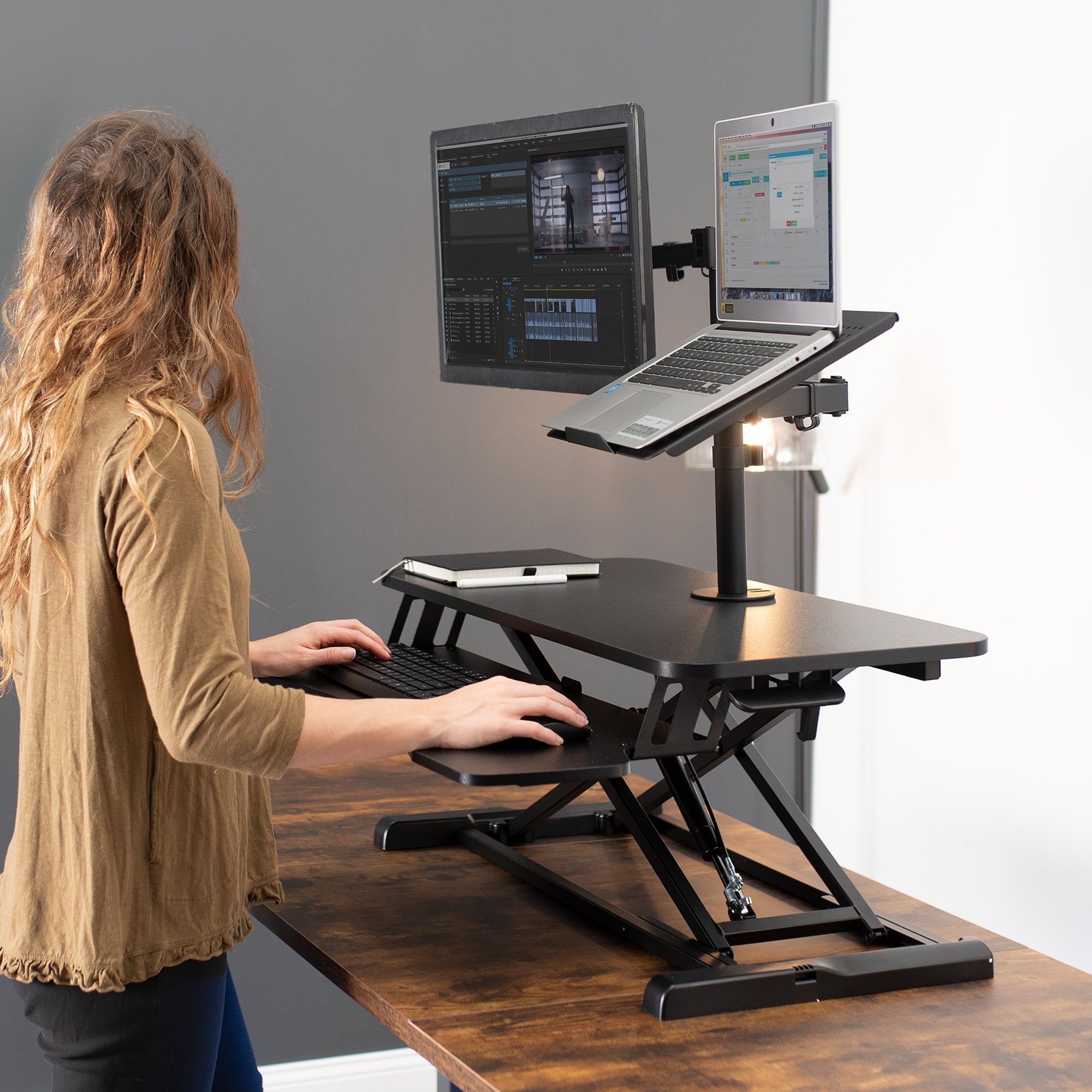 A woman using a sit-to-stand table top desk converter to work while standing.